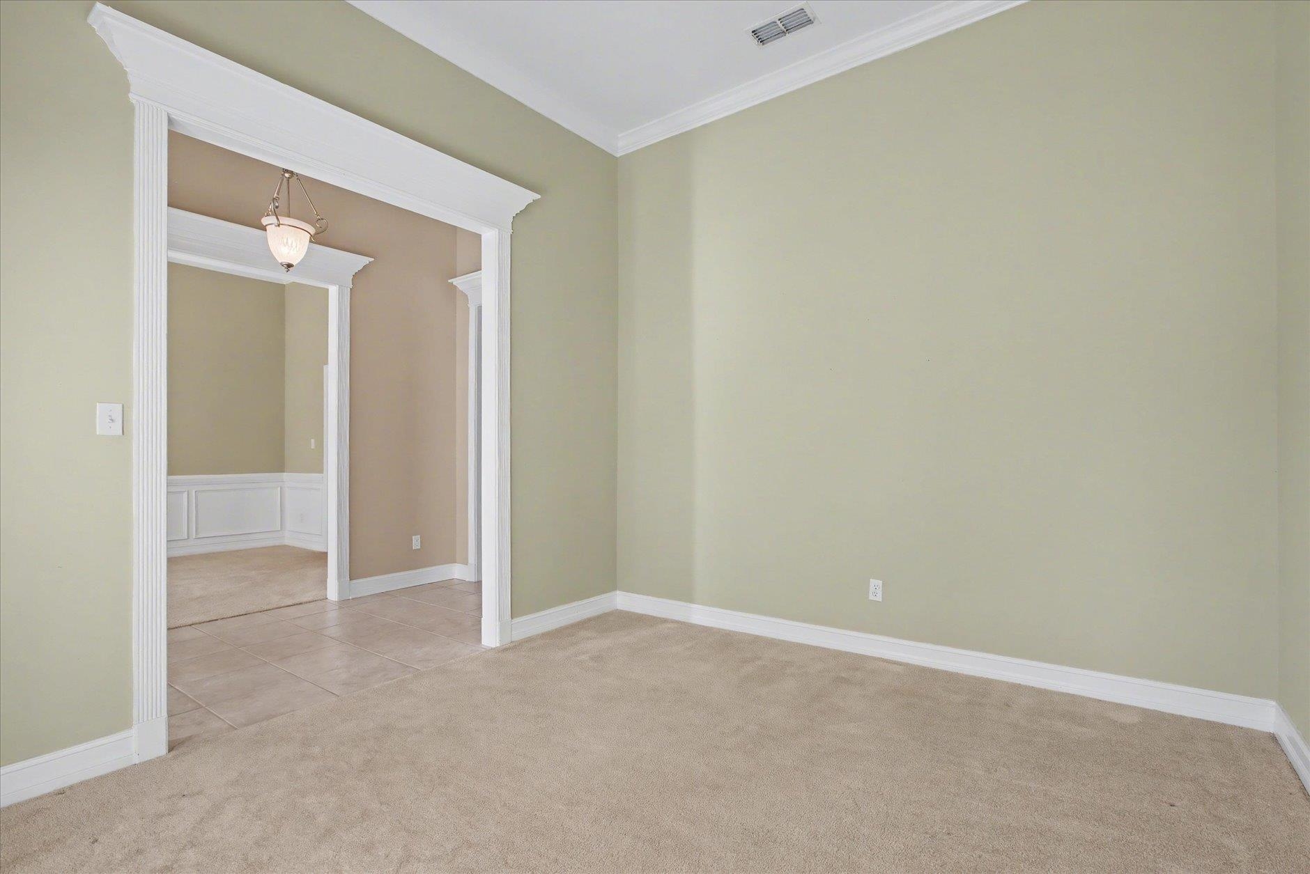 Empty carpeted room with pale green walls and a wide ornate opening to an adjoining tiled room.