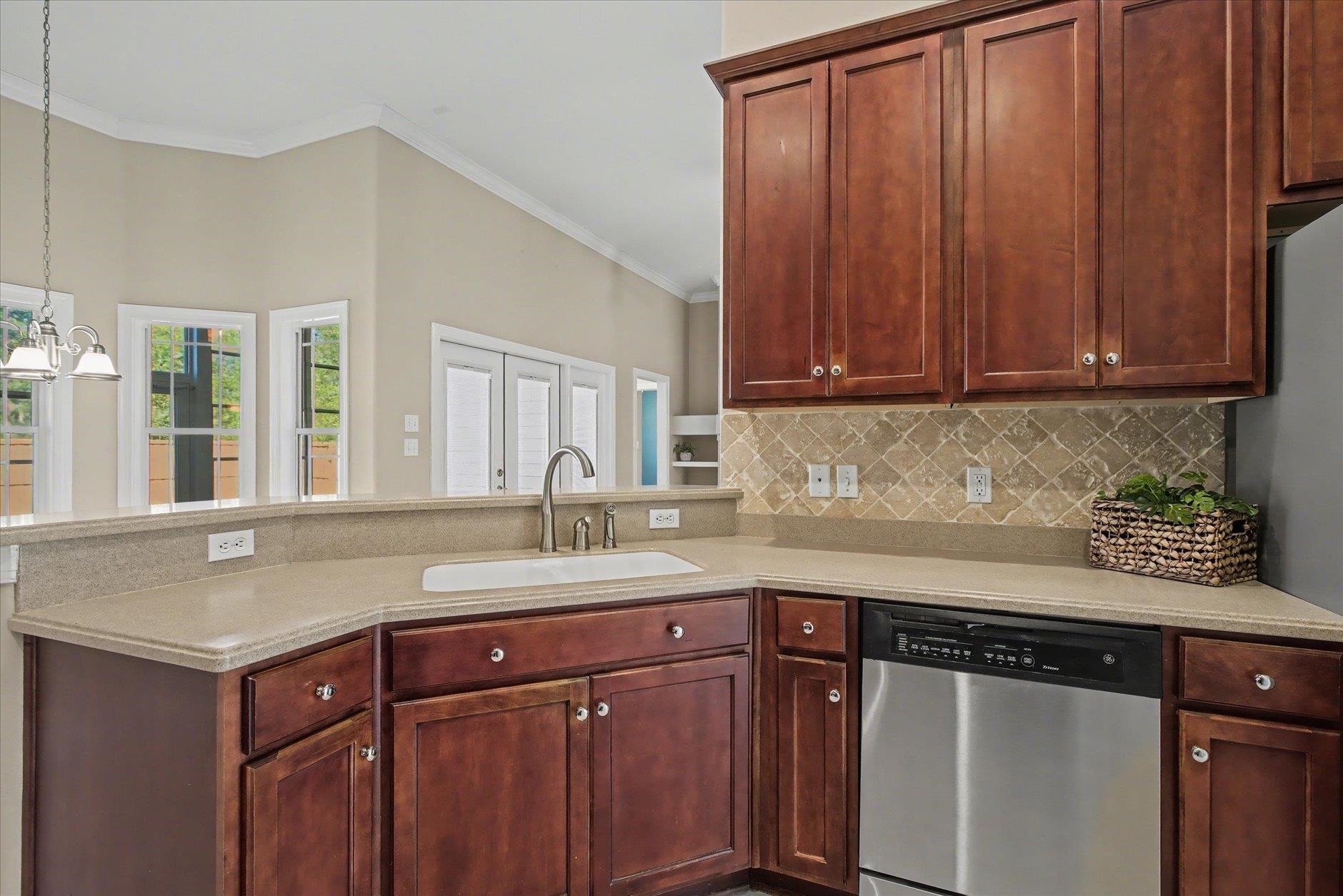 Kitchen with dark wood cabinets, beige counters, tiled backsplash, and stainless-steel dishwasher.