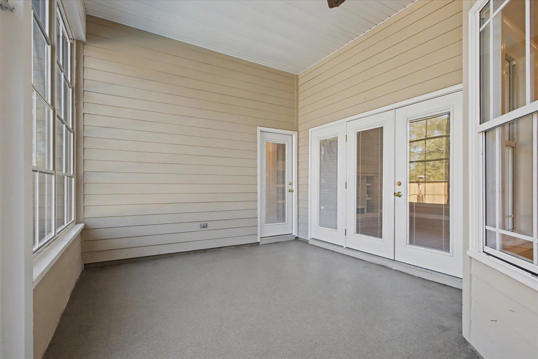 Empty enclosed porch with gray carpet, large windows, and white glass-paneled doors.