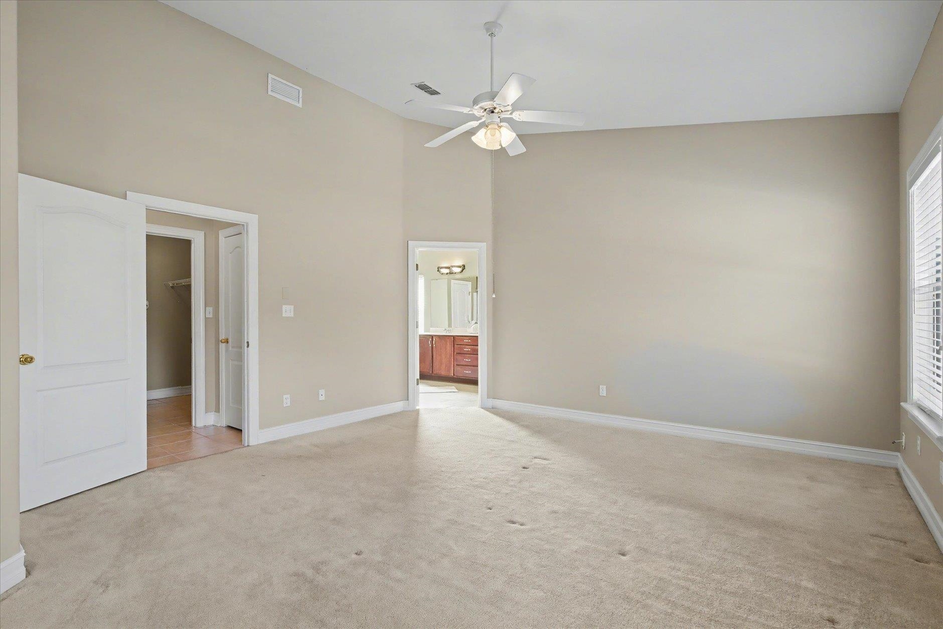 Empty carpeted bedroom with a vaulted ceiling, ceiling fan, and doorway to a bathroom.