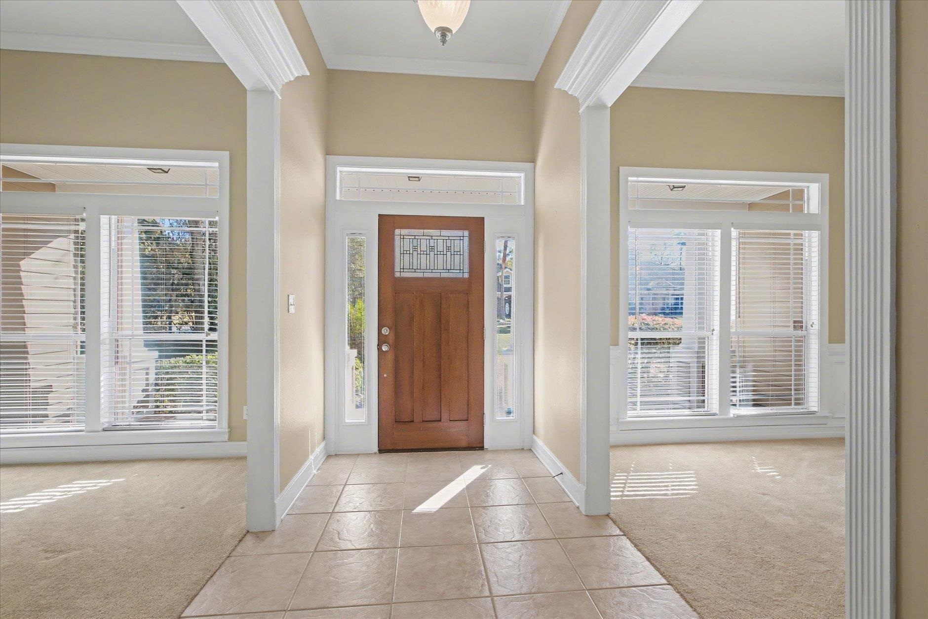 Entry foyer with a decorative glass wood door, sidelights, tiled floor, and carpeted rooms on either side.