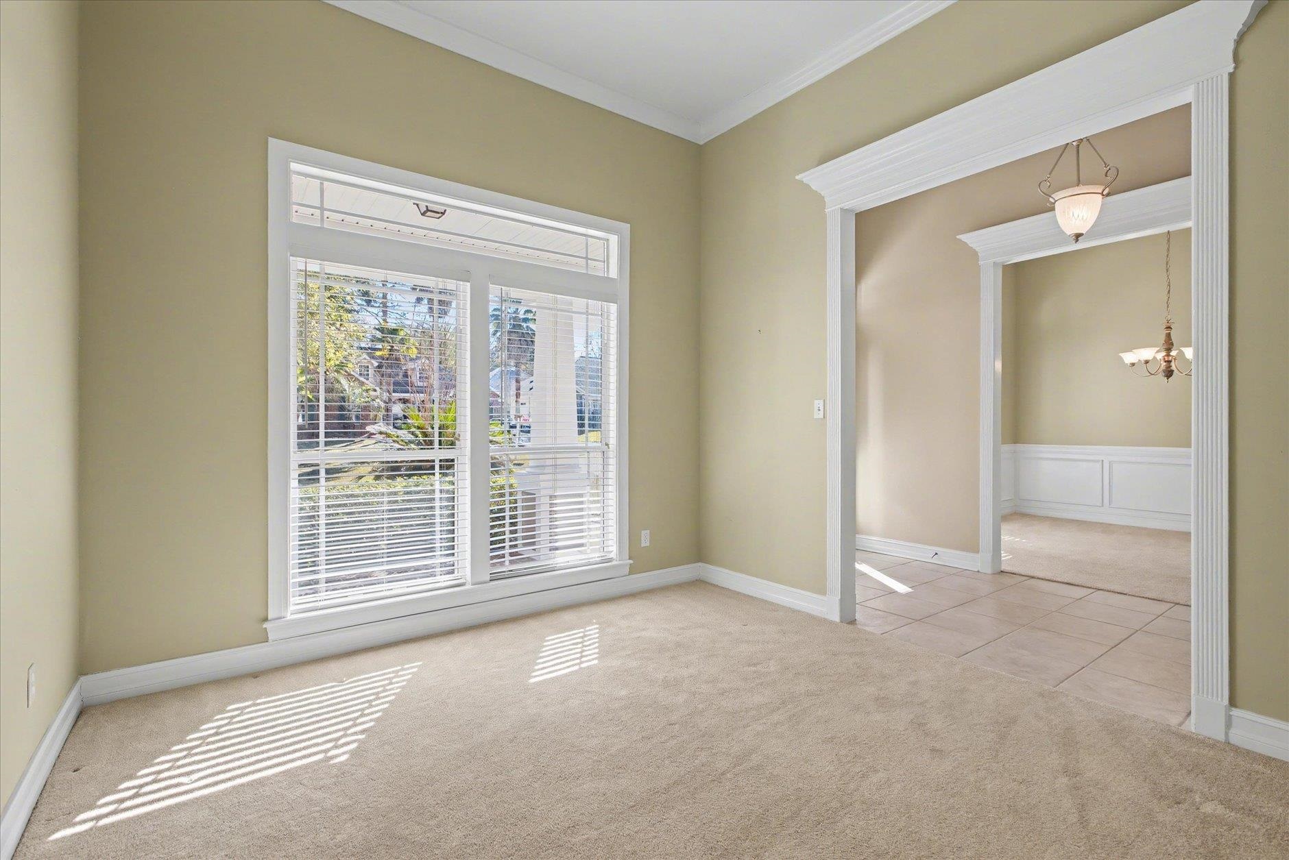 Empty carpeted living room with a large window and wide doorway to a tiled room.