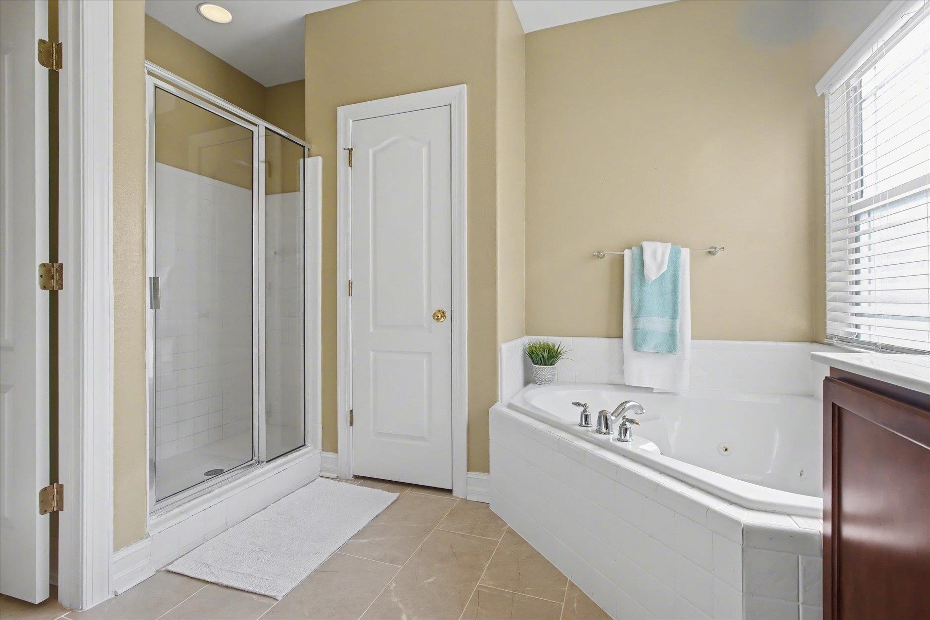 Bathroom with a glass shower and large jetted tub beneath a window with white blinds.