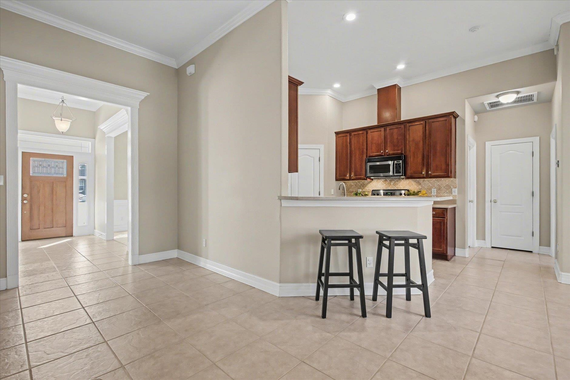 Kitchen with dark wood cabinets, a breakfast bar with two stools, and beige tile flooring.