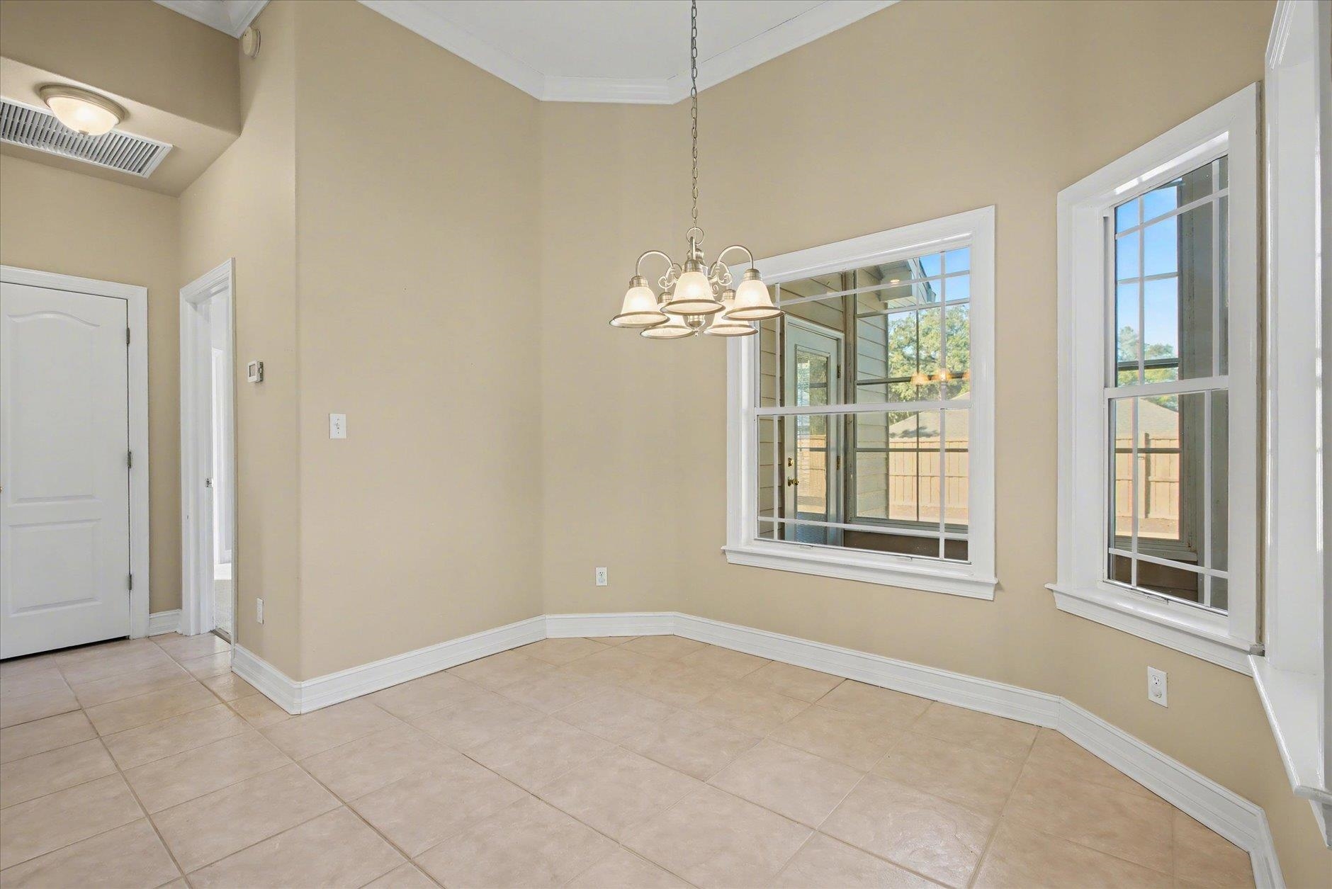 Empty dining area with tiled floors, a chandelier, and two windows overlooking a fenced yard.