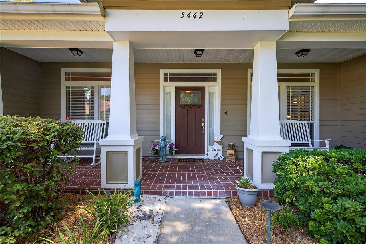 Home entrance with a covered brick porch, white columns, rocking chairs, and dark red front door.