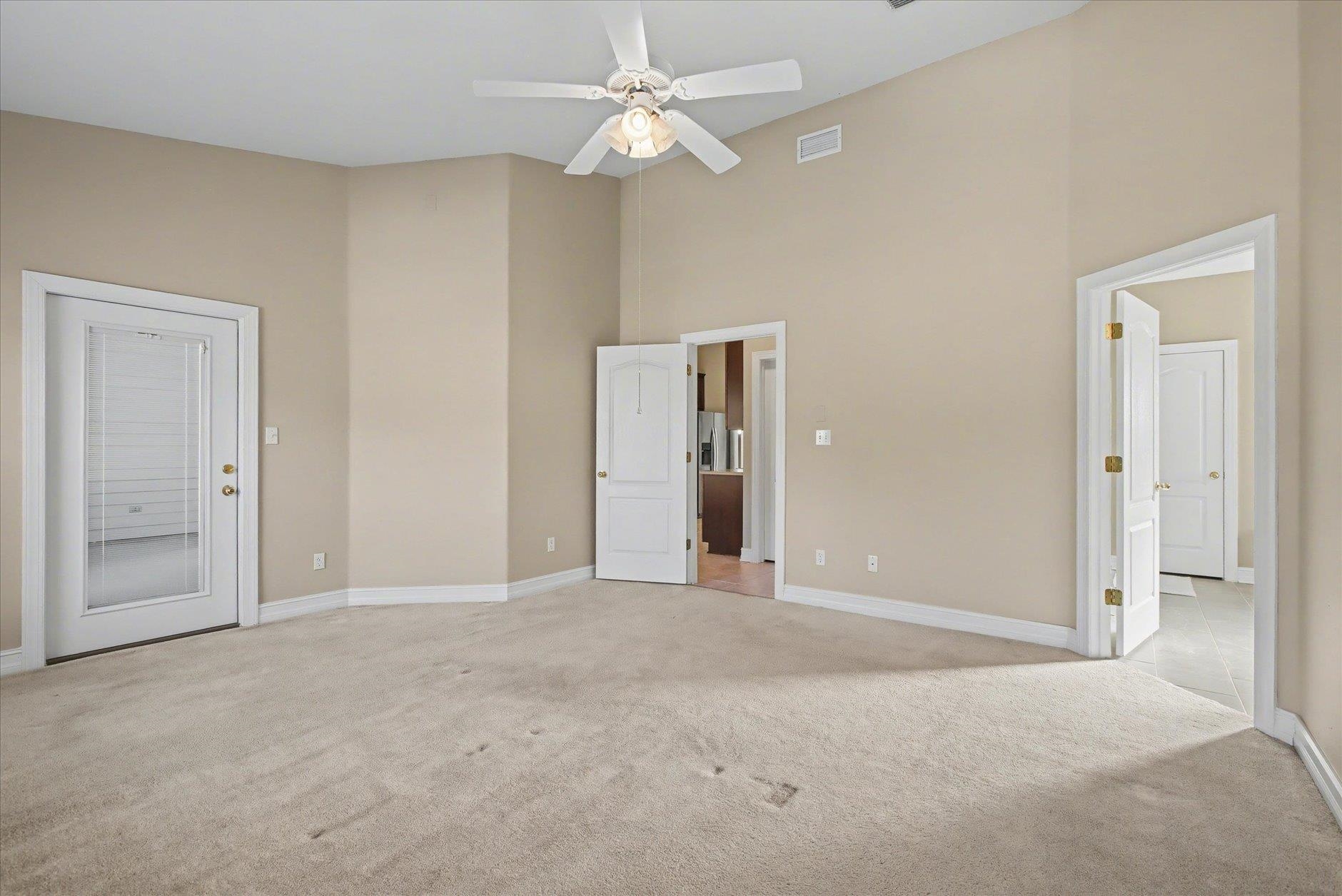 Empty bedroom with beige walls, light carpet, and a white ceiling fan.