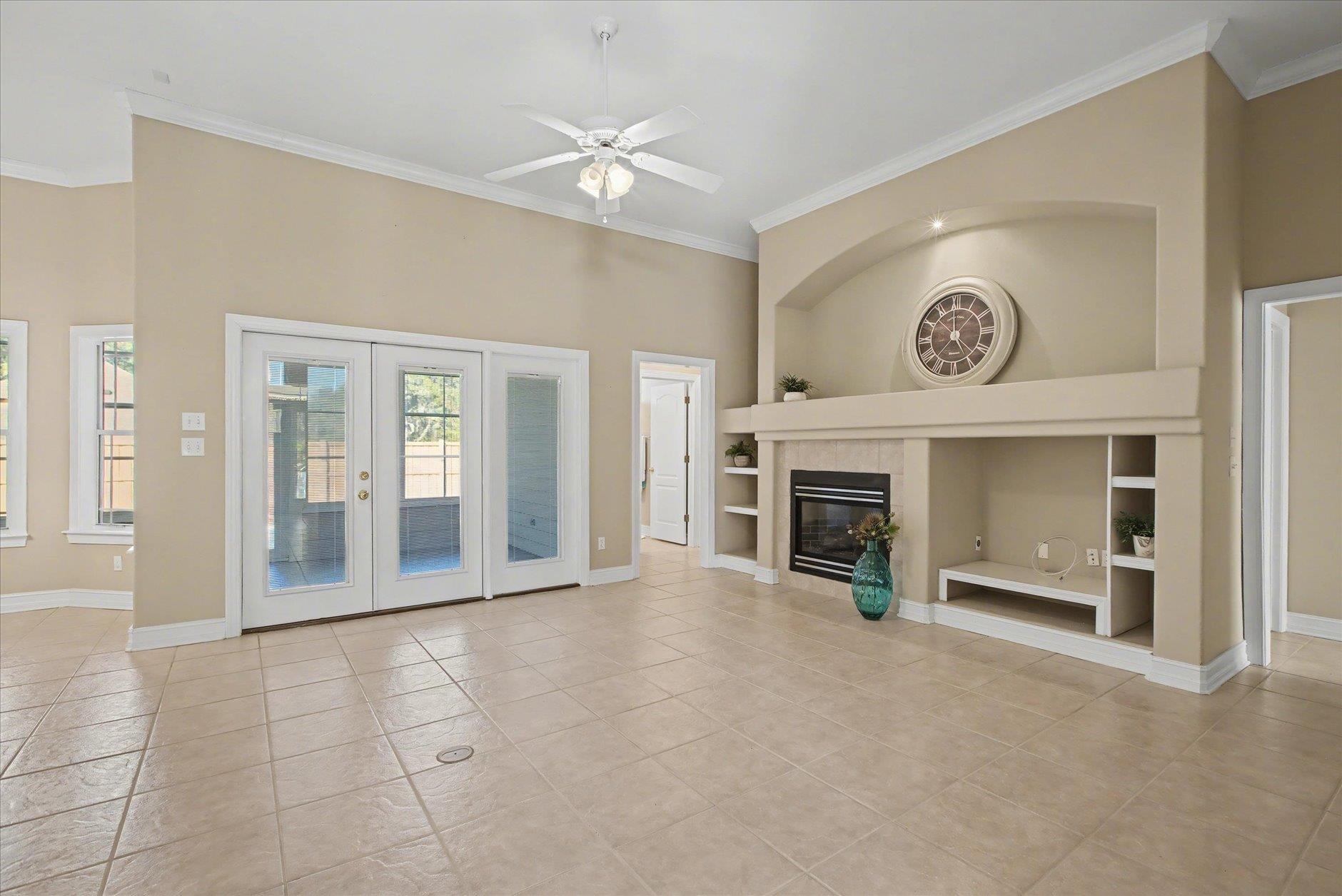 Empty living room with tiled floors, French doors, and a built-in fireplace beneath a large clock.