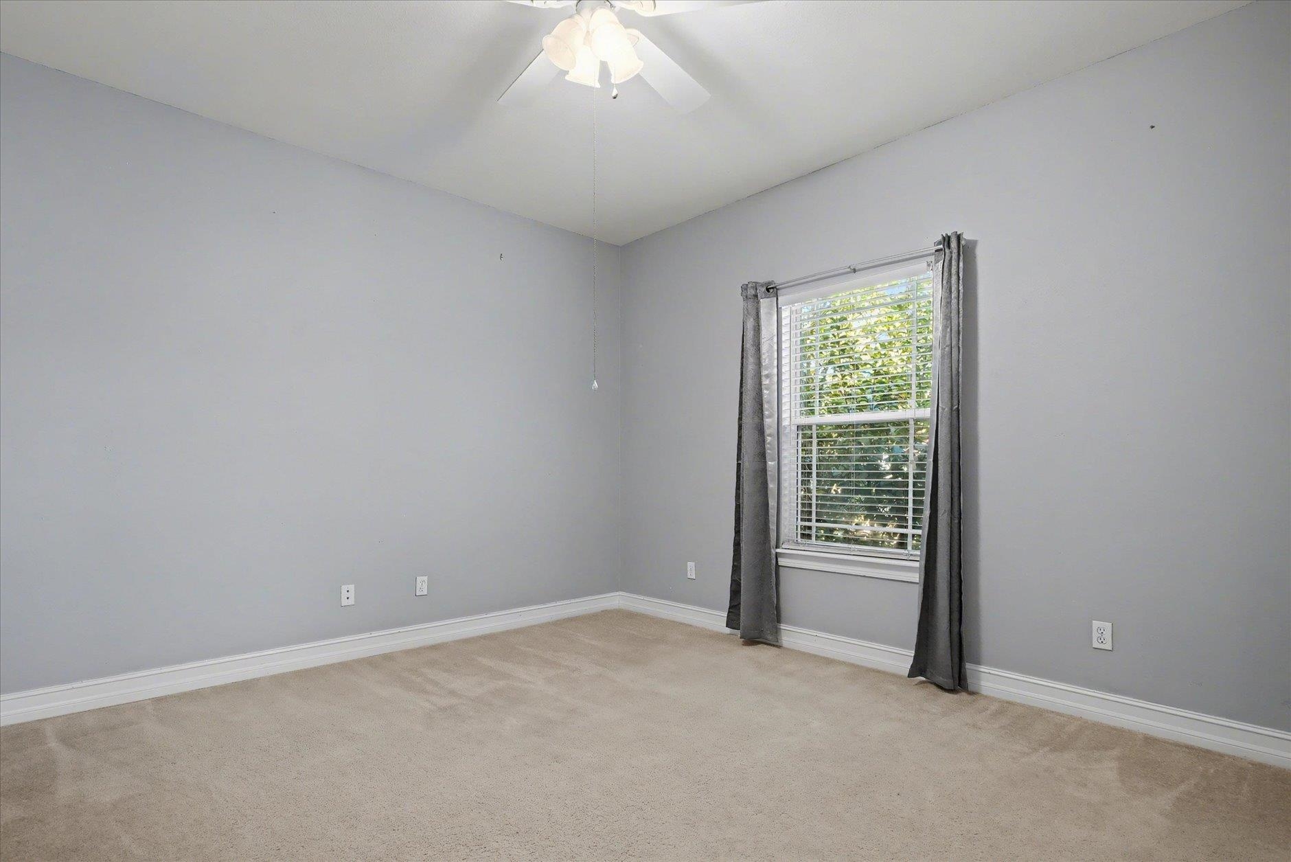 Empty bedroom with beige carpet, gray walls, and a curtained window.