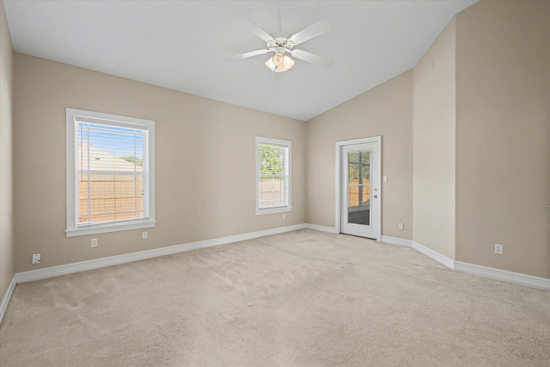 Empty carpeted room with two windows, a glass-paneled exterior door, and a ceiling fan.