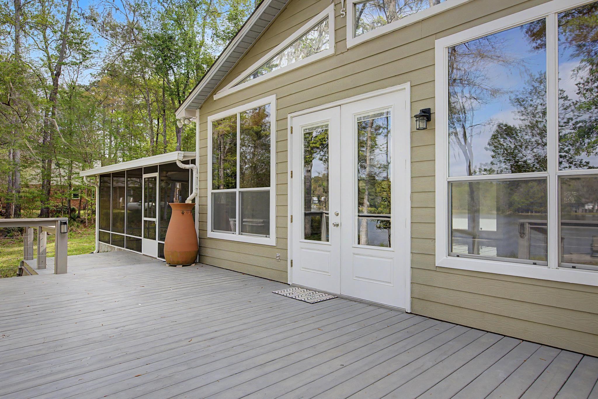 Home’s rear deck with white-trimmed doors, screened porch, and terracotta chiminea among trees.
