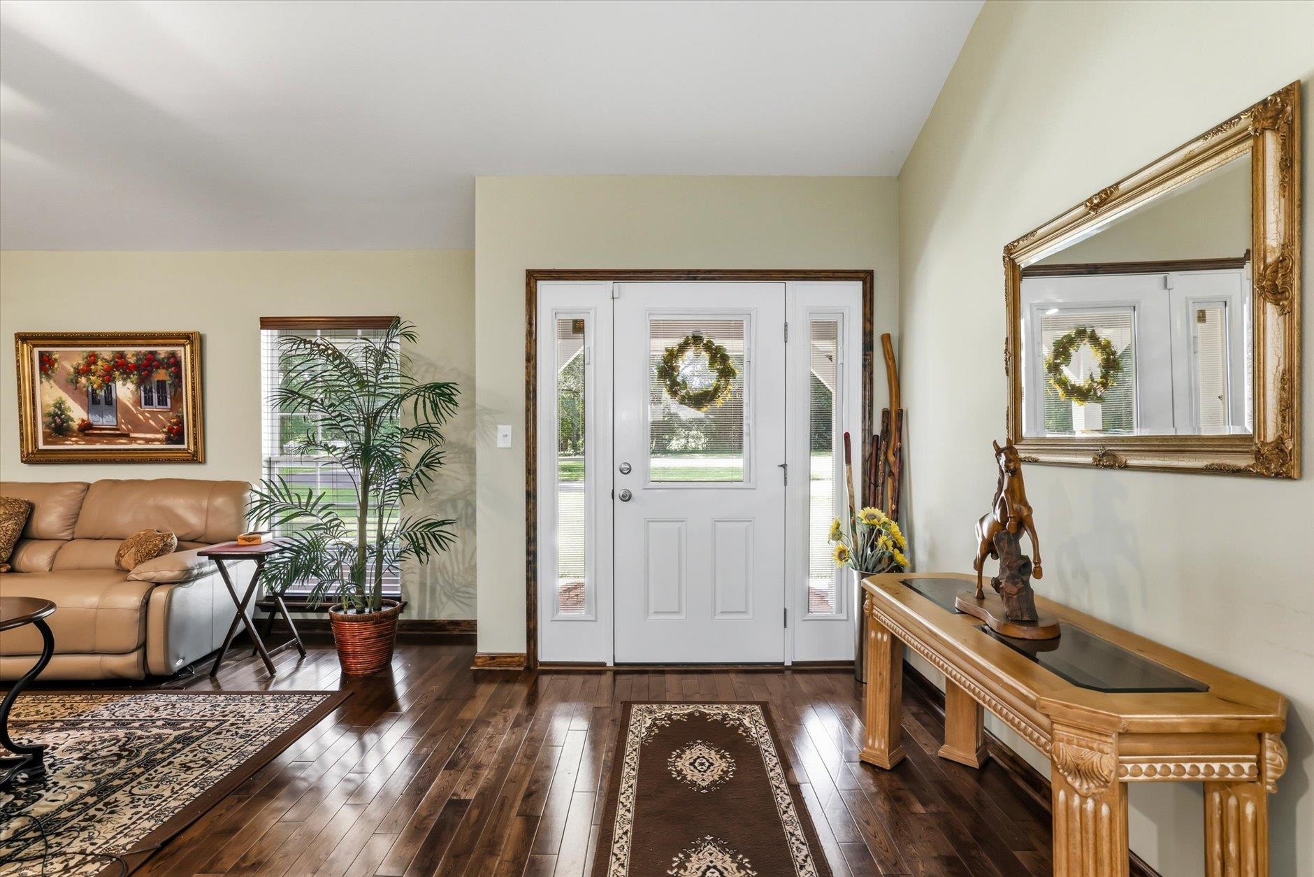 Furnished entryway with a white front door, dark hardwood floors, tan sofa, and ornate wood furniture.