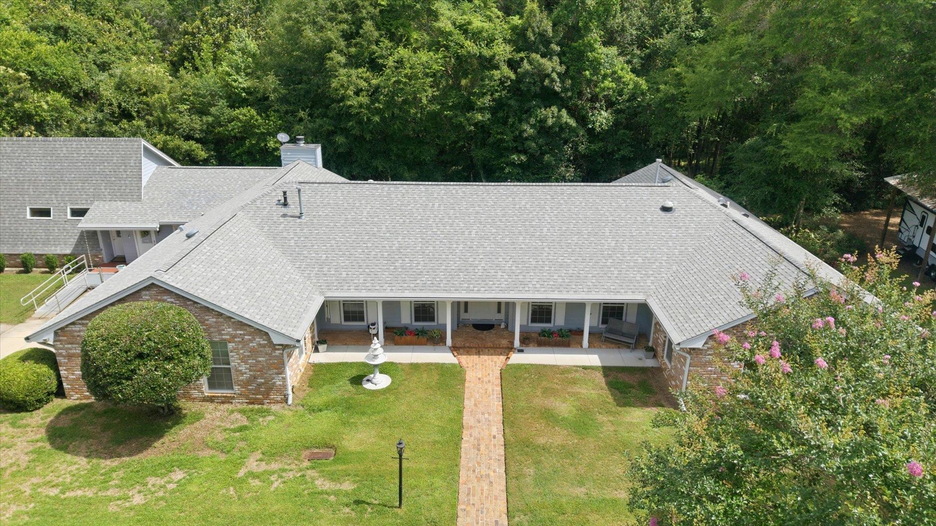 Aerial view of a brick home with a broad gray roof, covered porch, and front lawn.