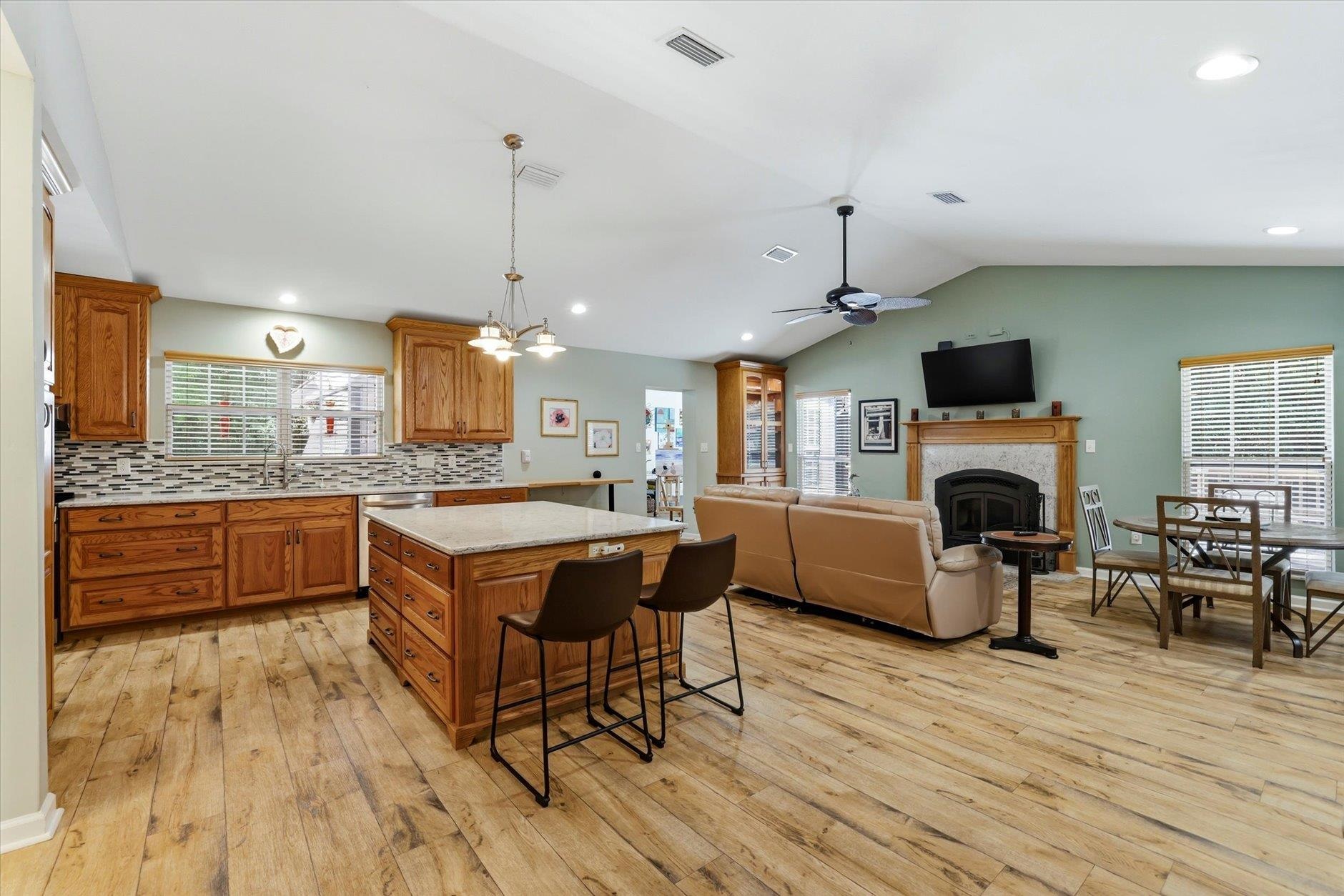 Open-plan kitchen and living room with a wood-cabinet island, tan sectional, and fireplace.