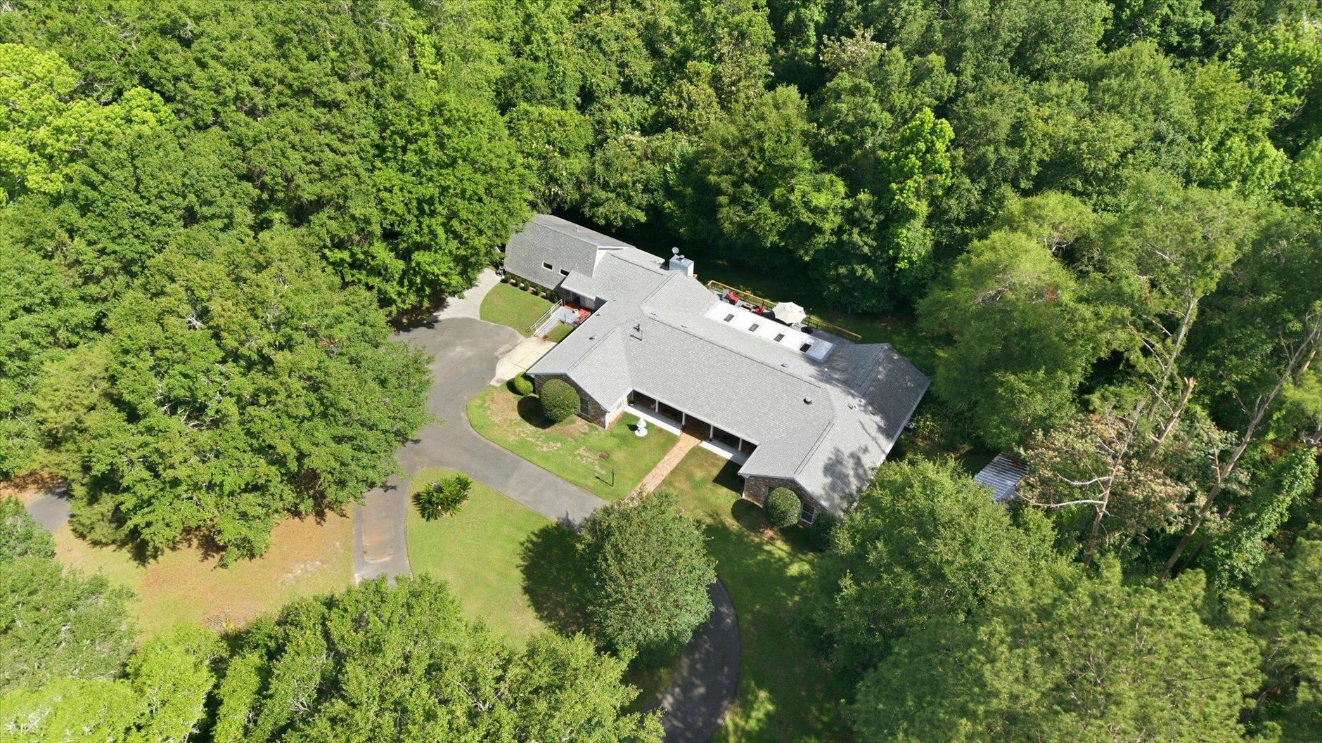 Aerial view of a gray-roofed home and curved driveway surrounded by dense trees.