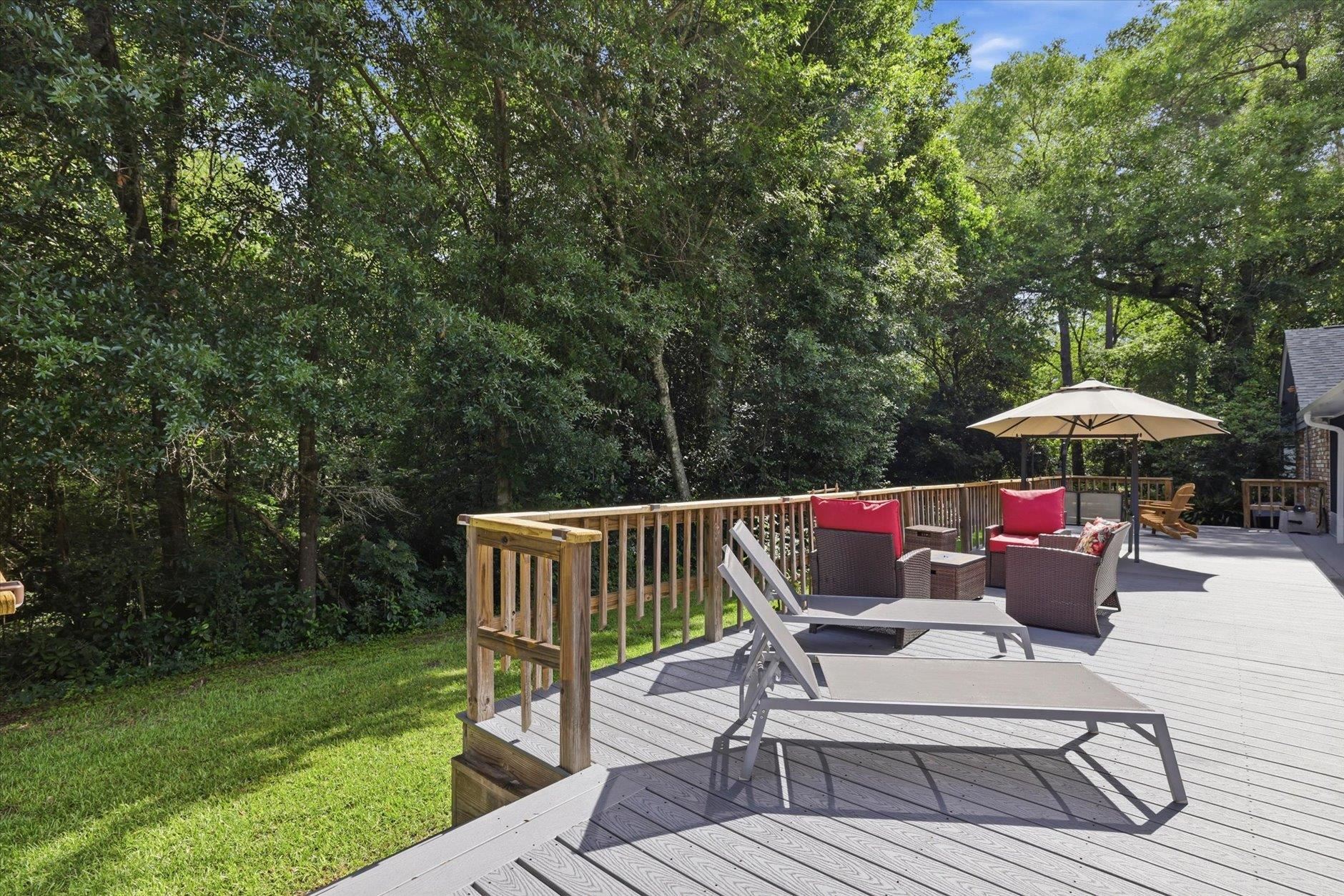 Spacious deck with lounge chairs and red-cushioned seating beside a wooded yard.