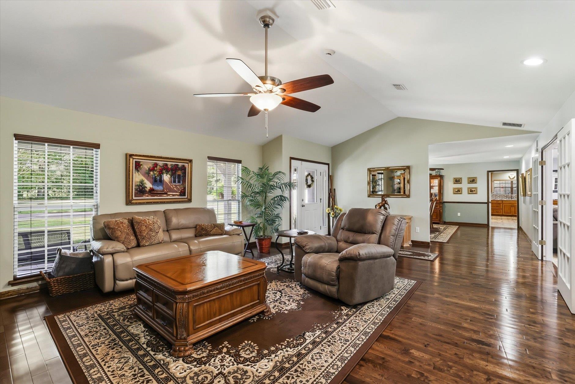 Furnished living room with a vaulted ceiling, leather seating, patterned rug, and dark wood floors.