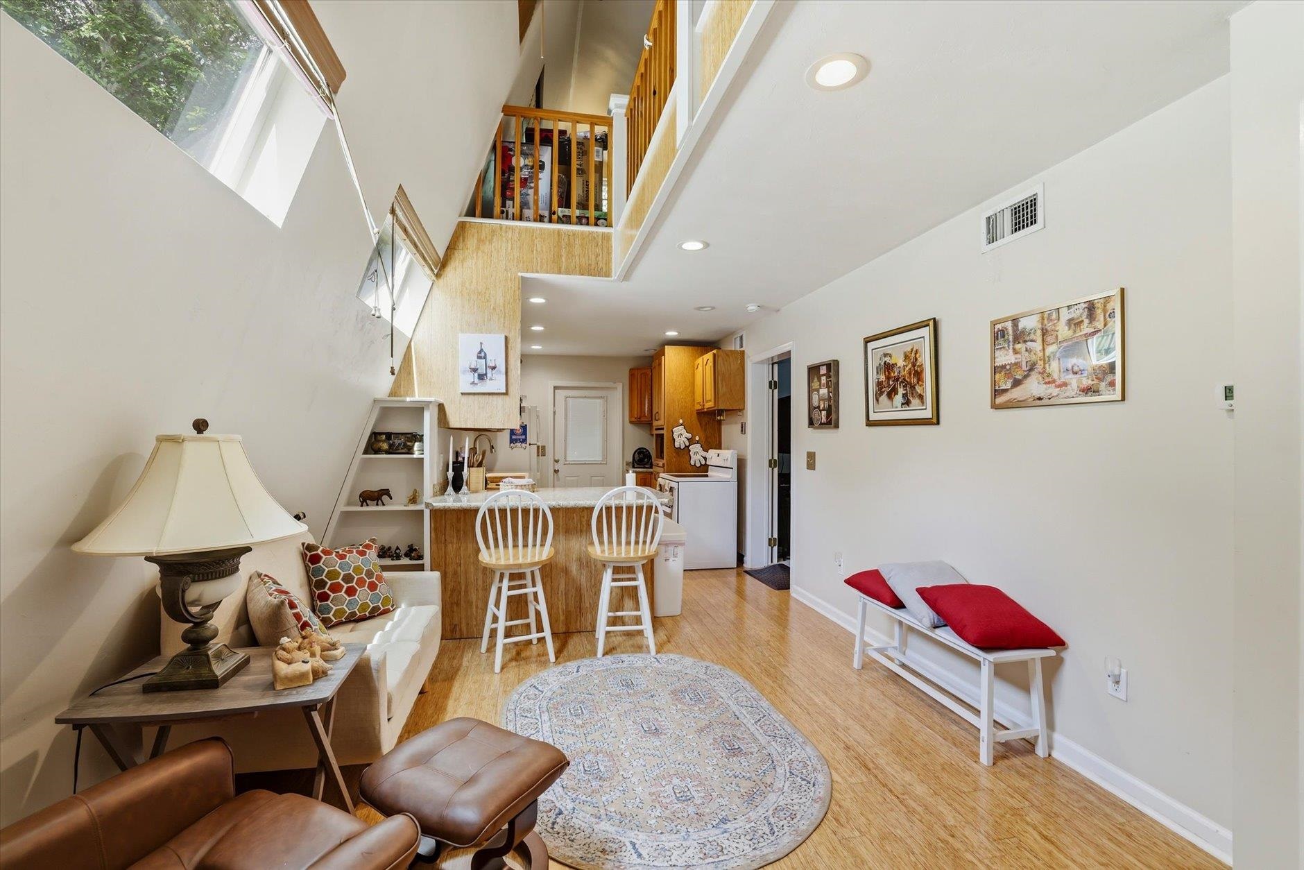 Living room with a kitchen breakfast bar, loft railing, tall windows, and wood flooring.