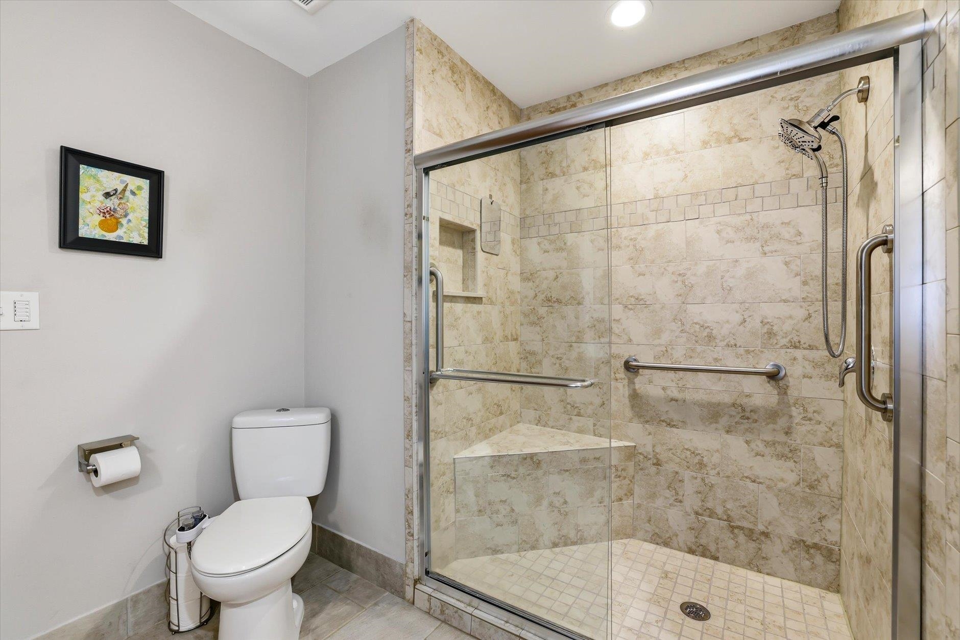Bathroom with a glass shower featuring beige tile, a built-in bench, and grab bars.