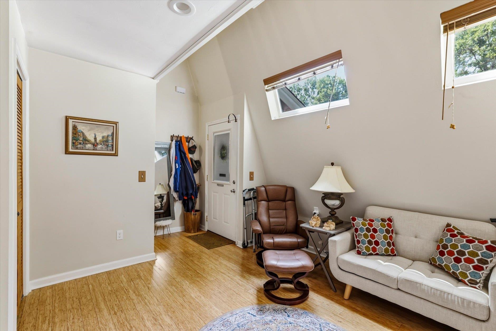 Living room with vaulted ceiling, angled clerestory windows, wood floors, and contrasting sofa and leather chair.