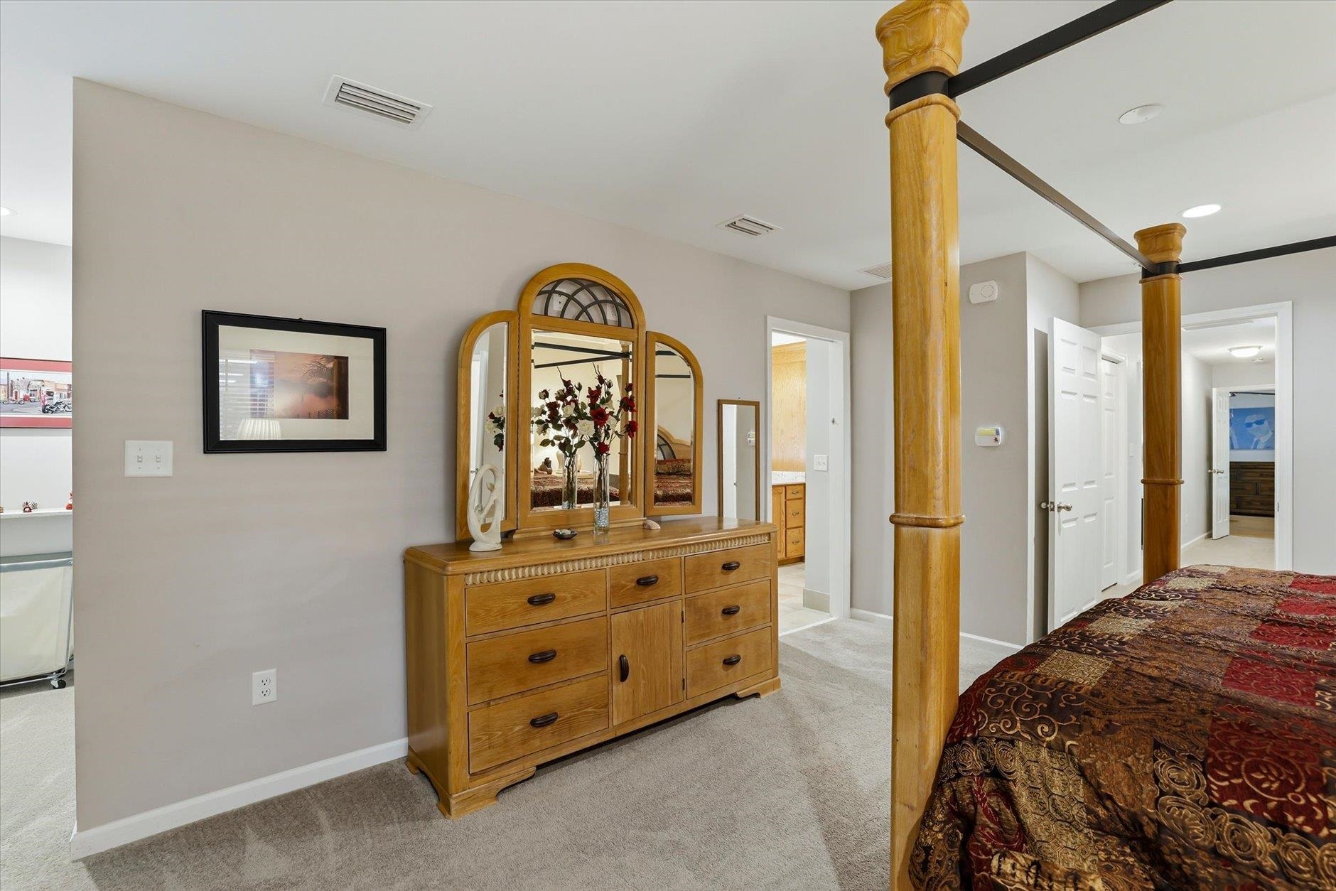 Furnished bedroom with a wooden four-poster bed and matching dresser with an arched mirror.