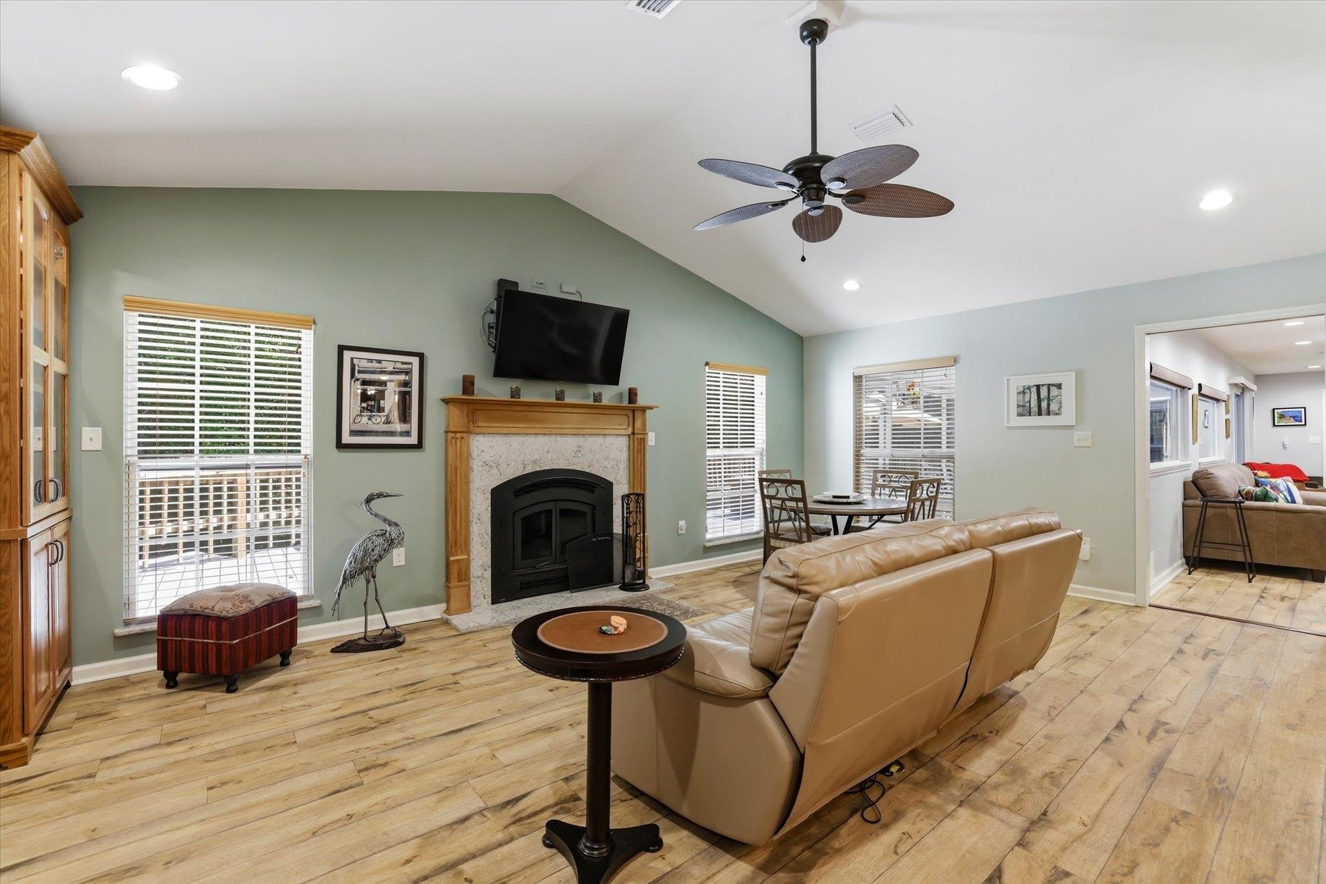 Living room with a fireplace, vaulted ceiling, tan leather sectional, and adjoining dining area.