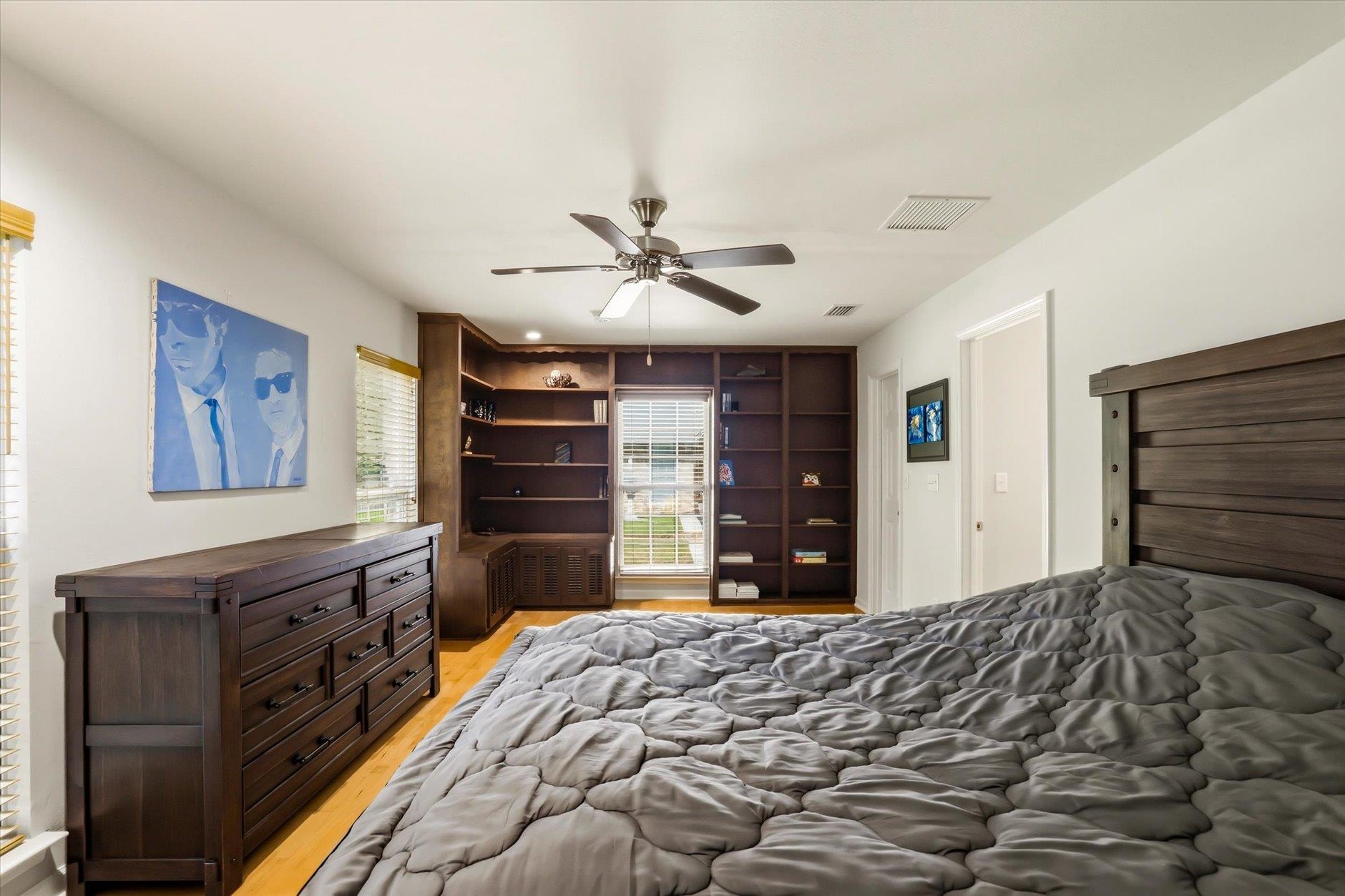 Bedroom with a gray quilted bed and dark wood built-in bookshelves.