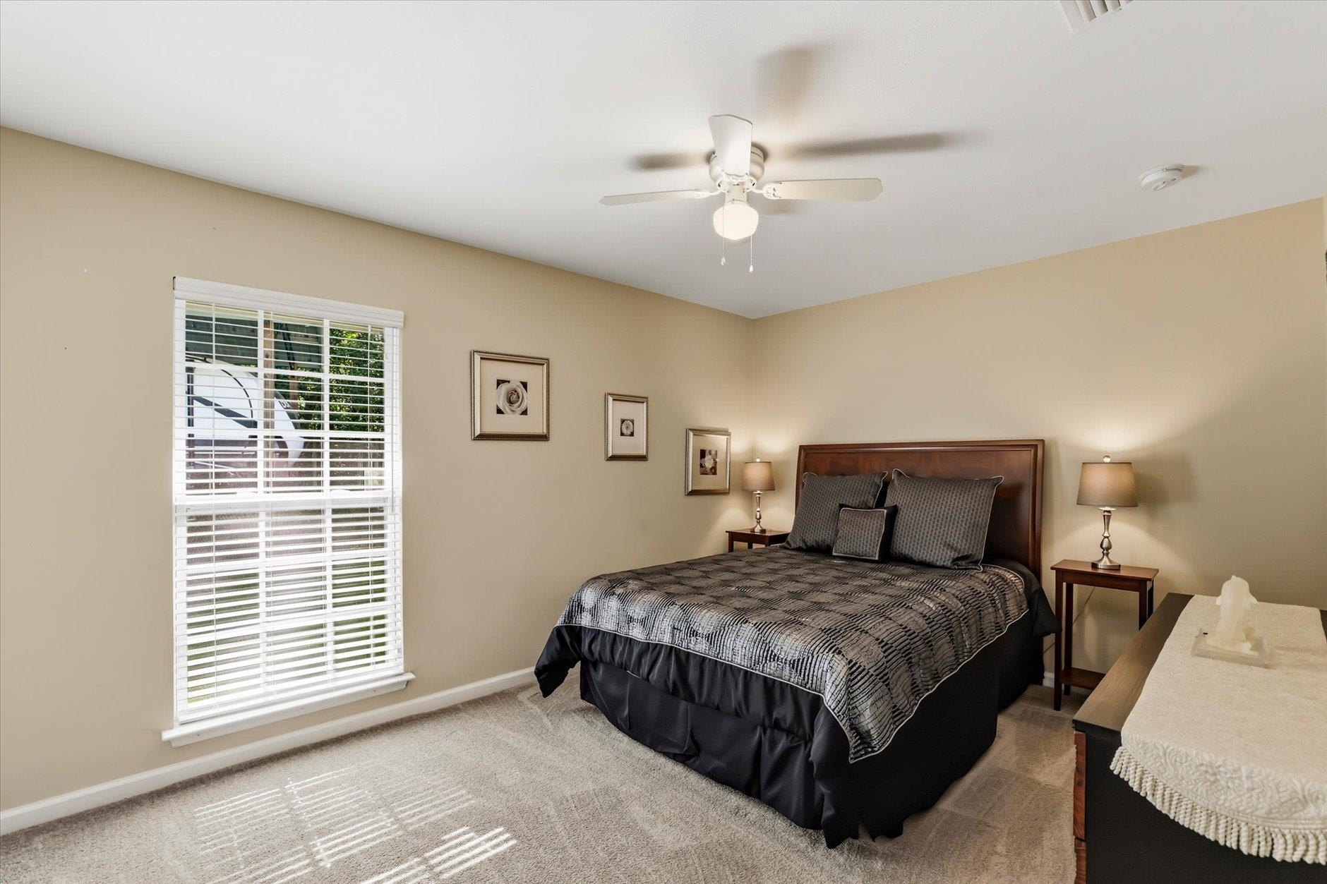 Bedroom with a dark wood bed, gray patterned bedding, and a large window with white blinds.