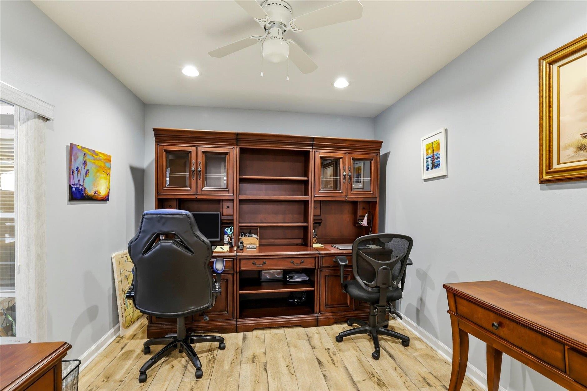 Furnished home office with dark wood built-in desk, shelving, and two office chairs.