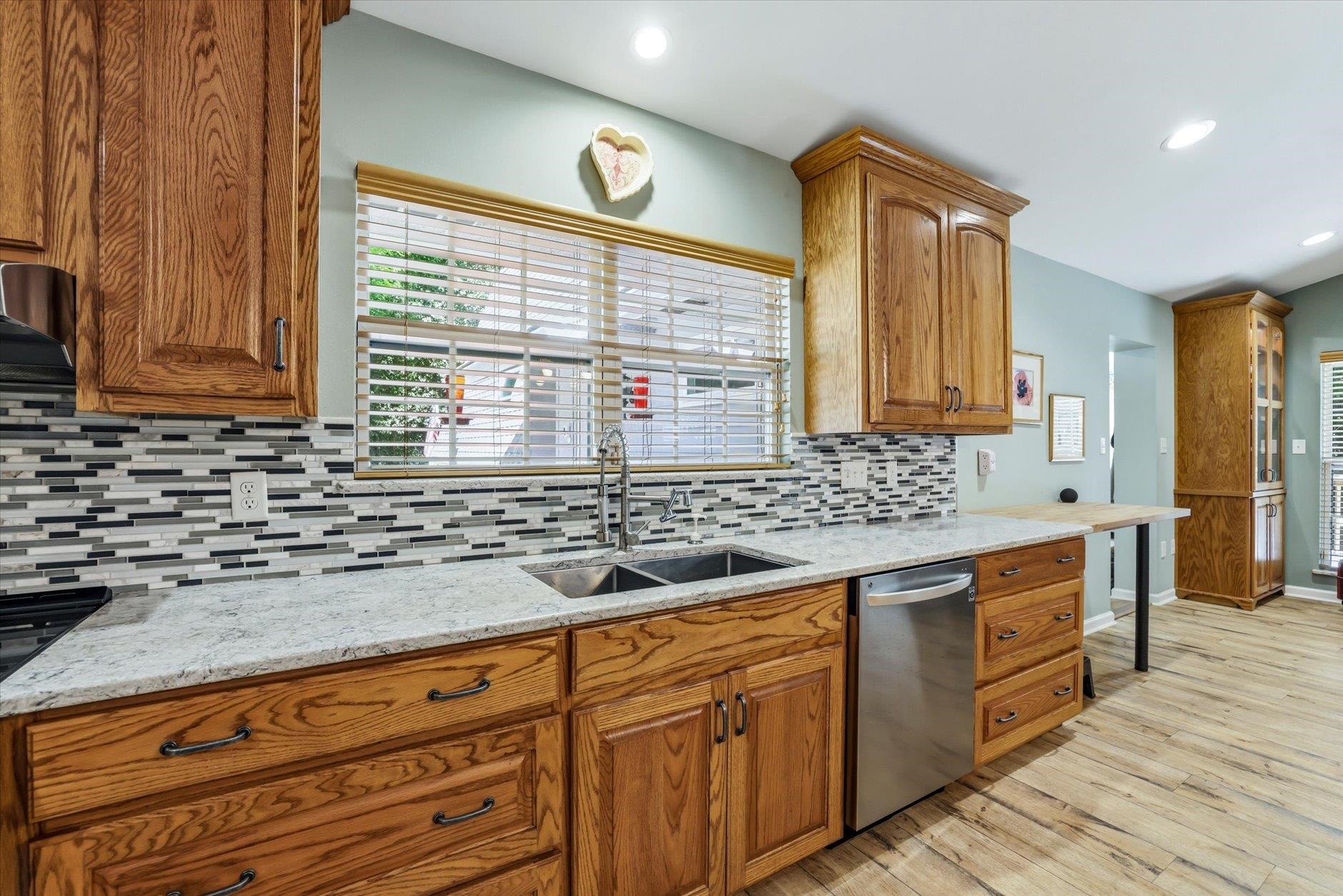 Kitchen with oak cabinets, granite counters, mosaic backsplash, and a double-basin sink beneath a window.