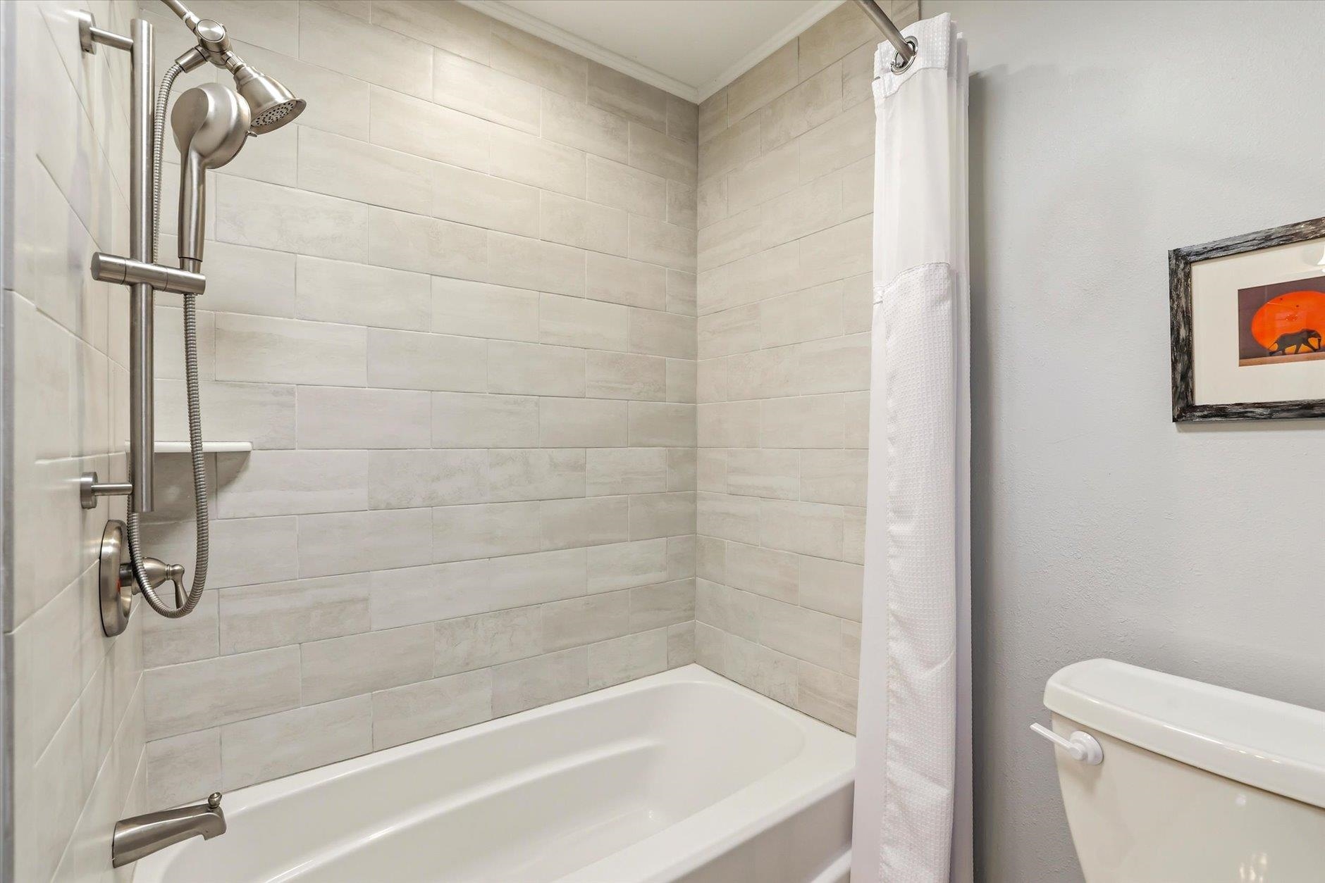 Bathroom with a white bathtub, pale tiled shower surround, and handheld showerhead.