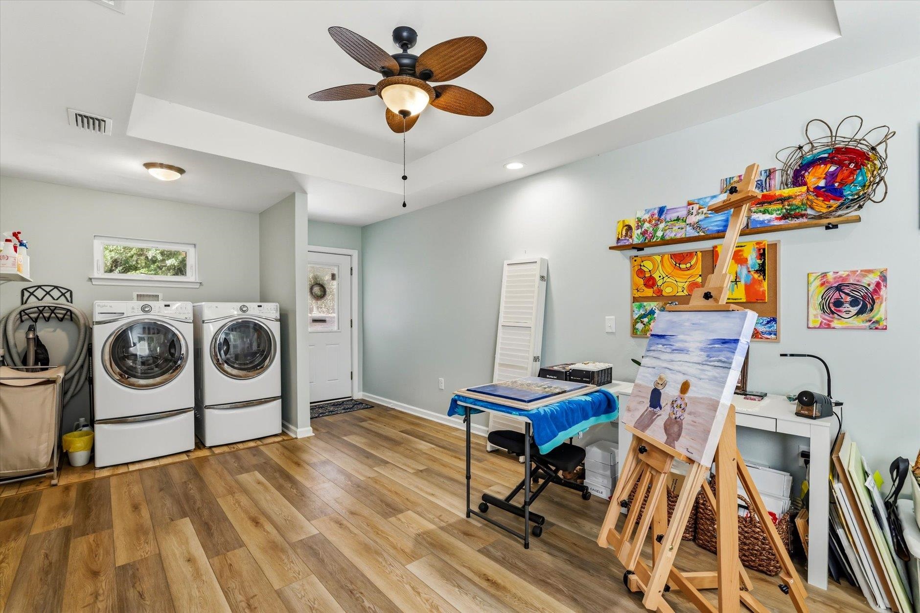Laundry and art studio with front-loading washer and dryer and colorful paintings on easels.