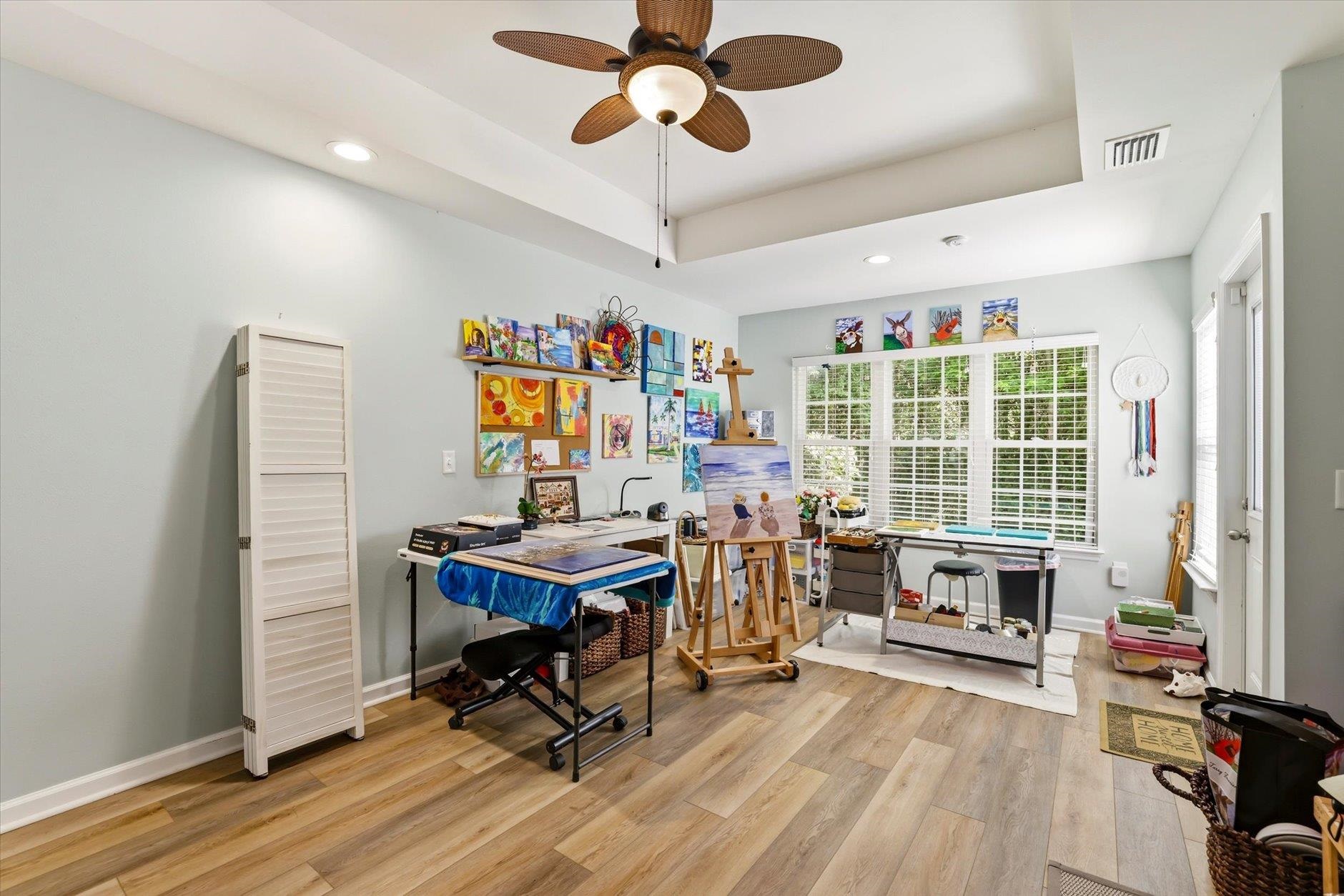Art studio with colorful wall paintings, easels, and worktables beside a large window.