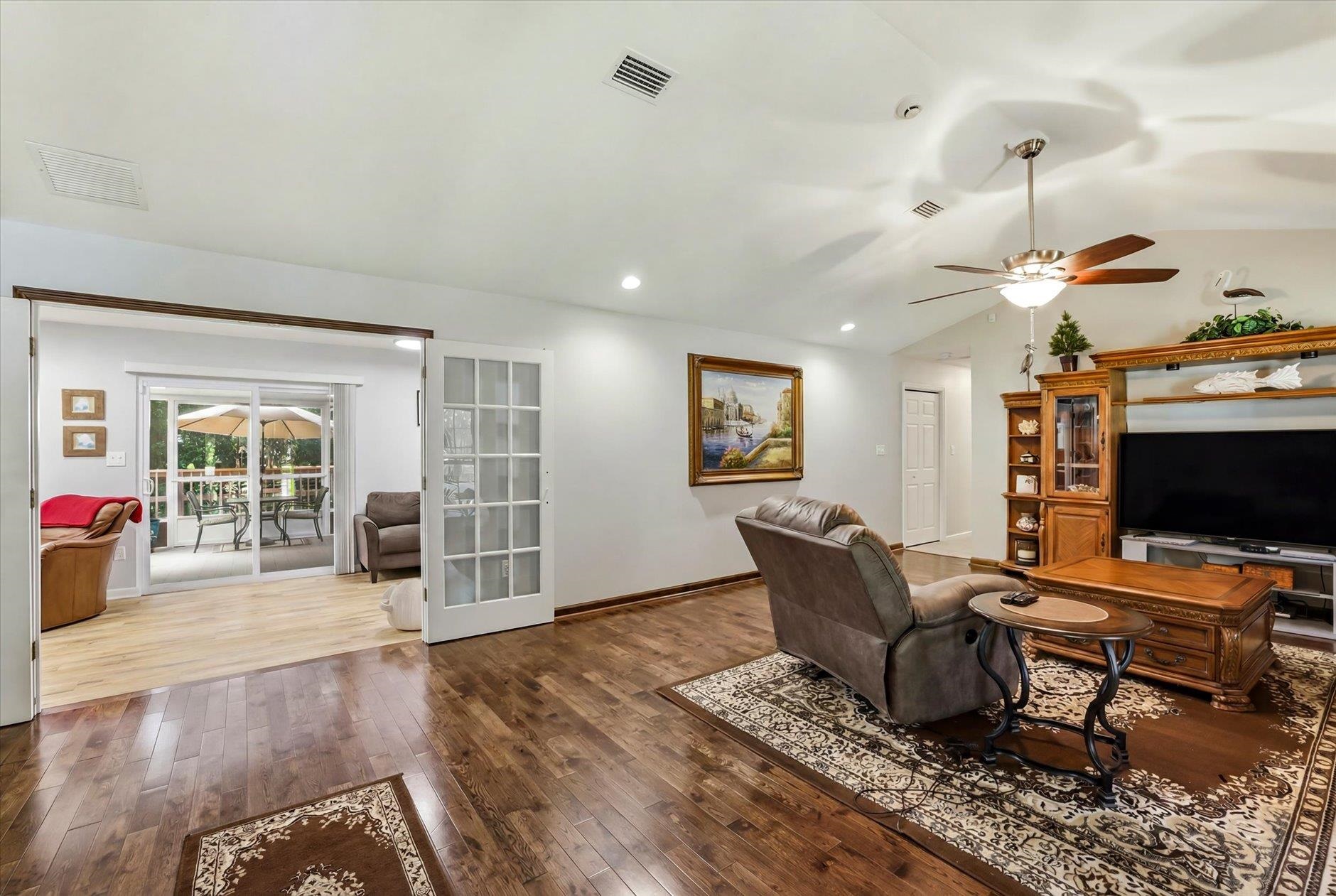 Living room with wood floors, a wooden entertainment center, and open French doors to a bright adjoining room.