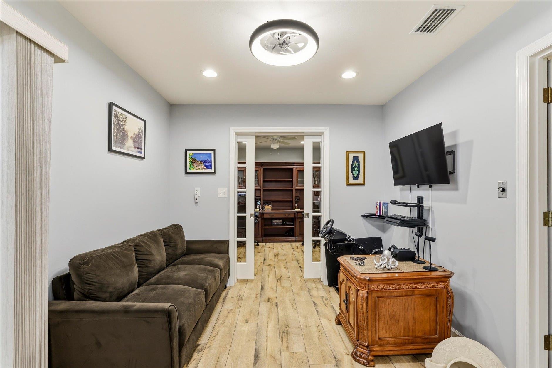 Furnished home office with a dark sectional sofa, wall-mounted TV, and sliding doors to built-in shelving.