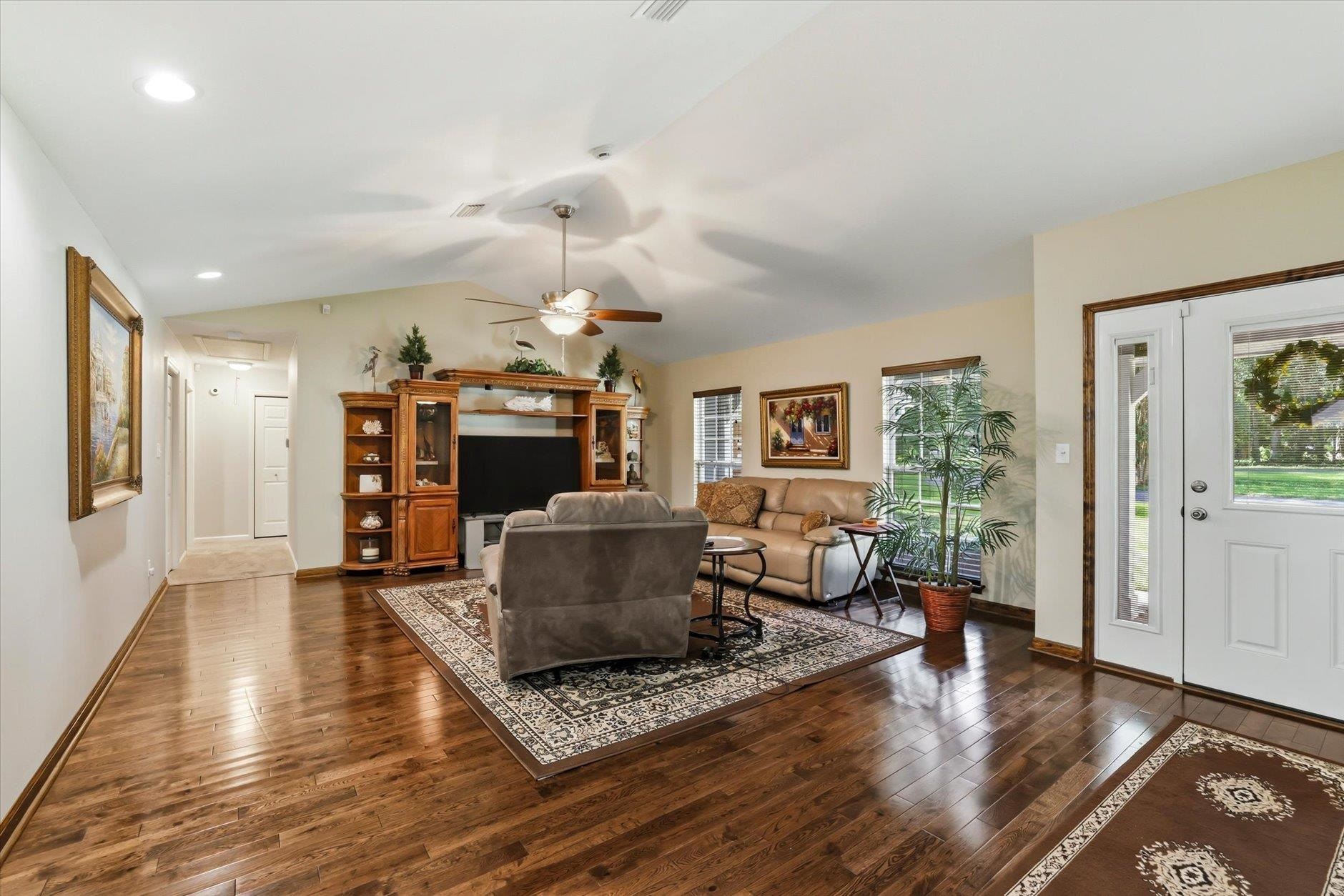 Furnished living room with hardwood floors, patterned rugs, and a large wooden entertainment center.