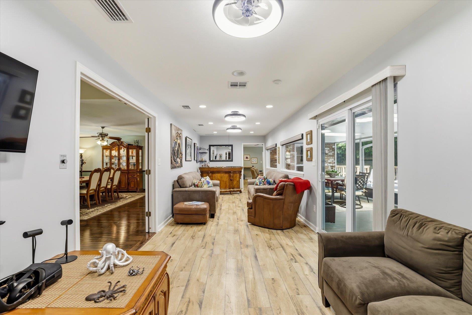Living room with leather seating, pale plank floors, and sliding doors to a patio.