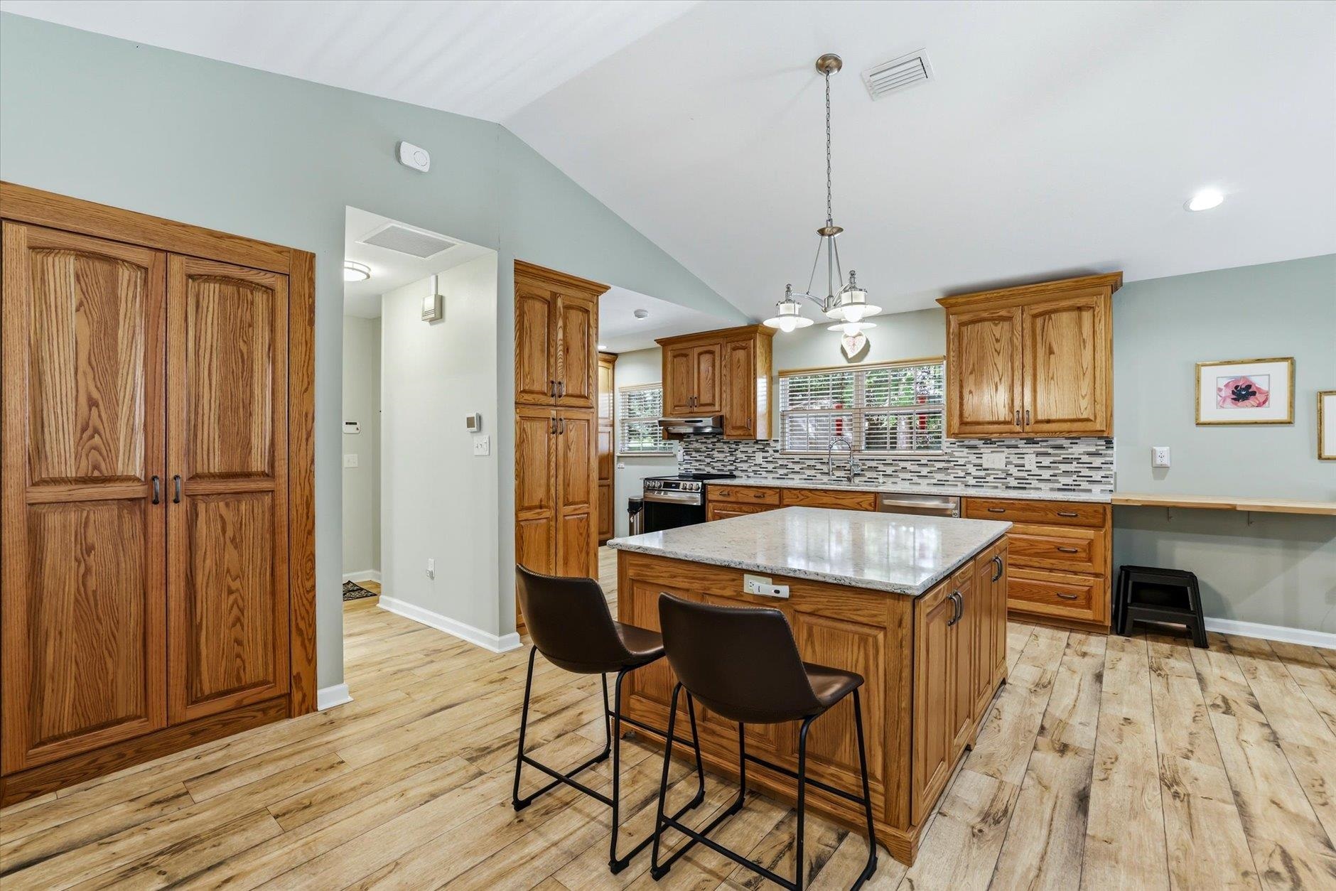 Kitchen with oak cabinetry, a large stone-topped island, mosaic backsplash, and light plank flooring.