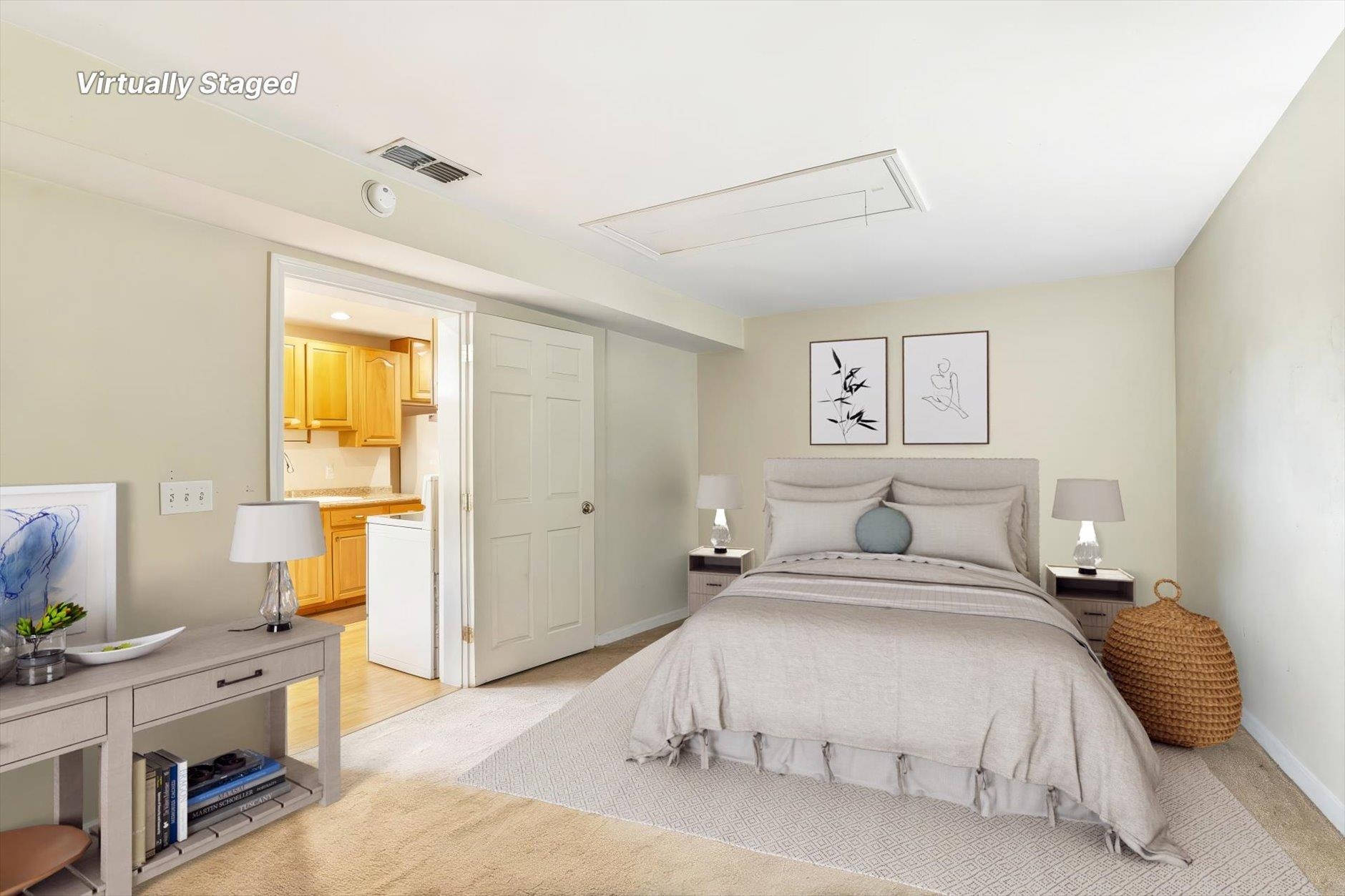 Virtually staged bedroom with a neutral bed, bedside tables, and a doorway to the kitchen.