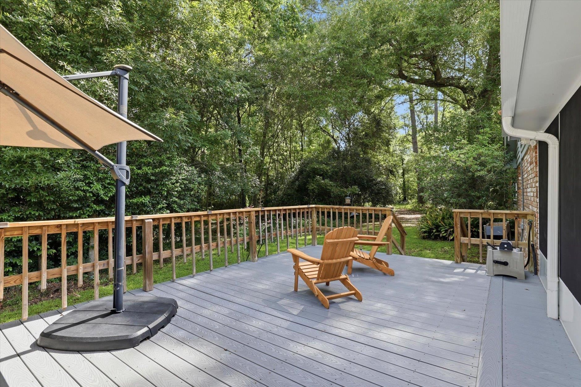 Back deck with Adirondack chairs and a shade umbrella, overlooking a wooded yard.