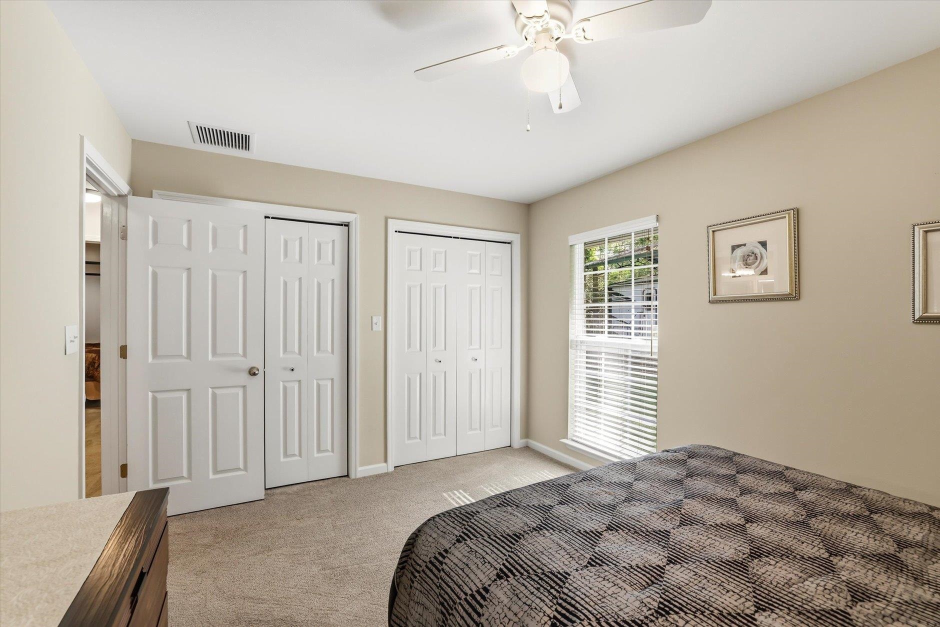Bedroom with a patterned bedspread, white closet doors, and a window with blinds.