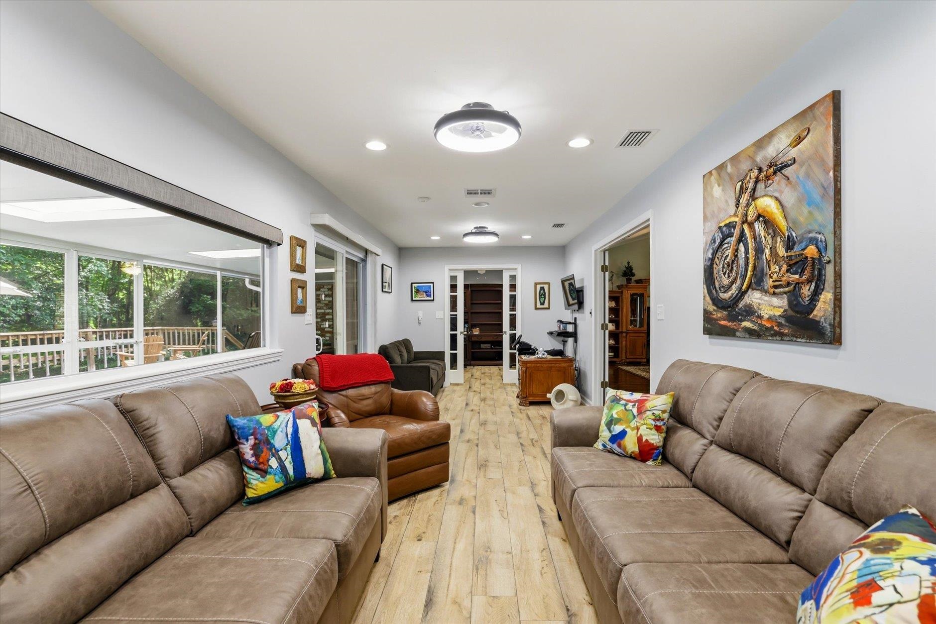 Living room with taupe seating, light wood-look floors, and a large window overlooking a wooded deck.