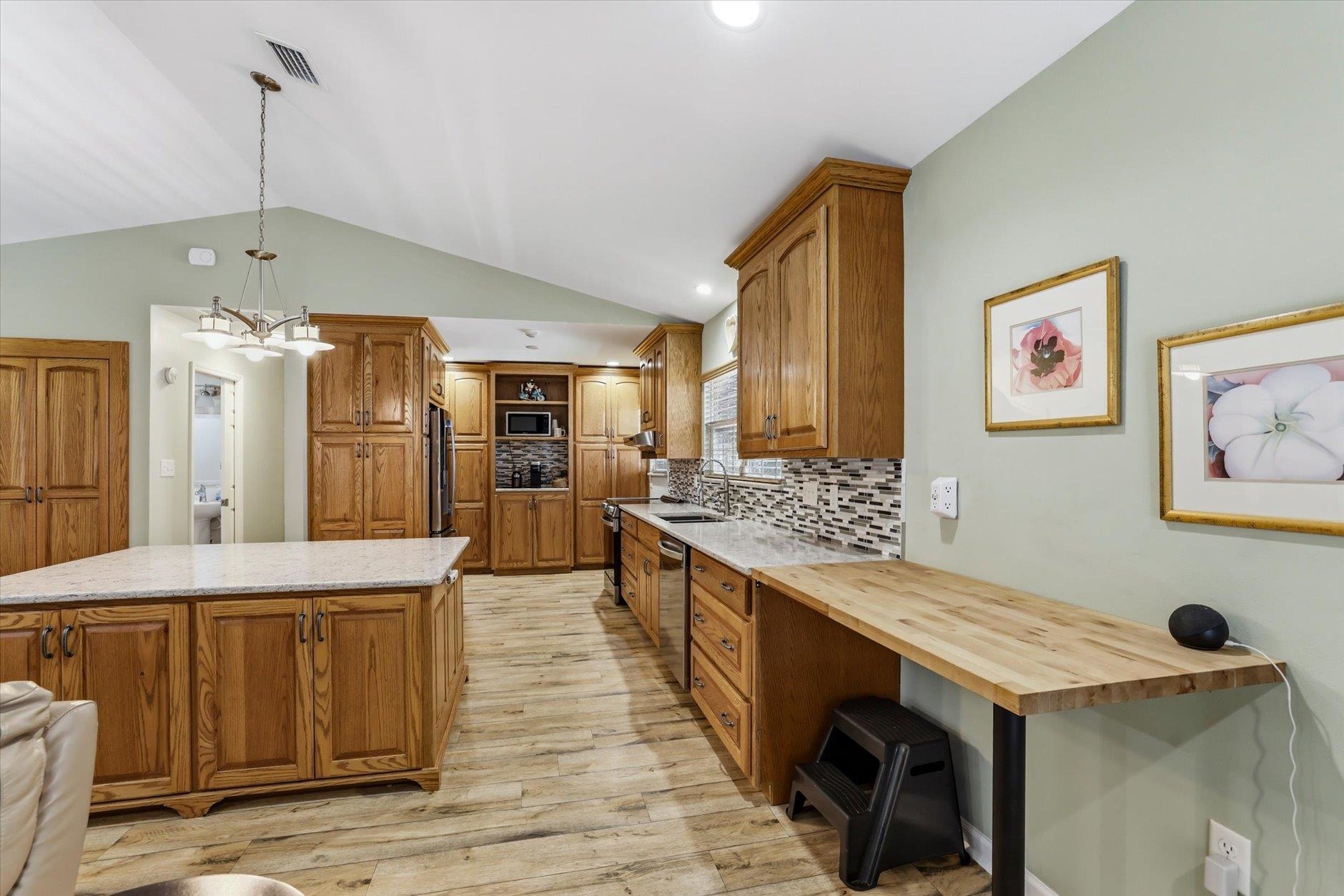 Kitchen with wood cabinetry, a large stone-topped island, mosaic backsplash, and butcher-block counter.