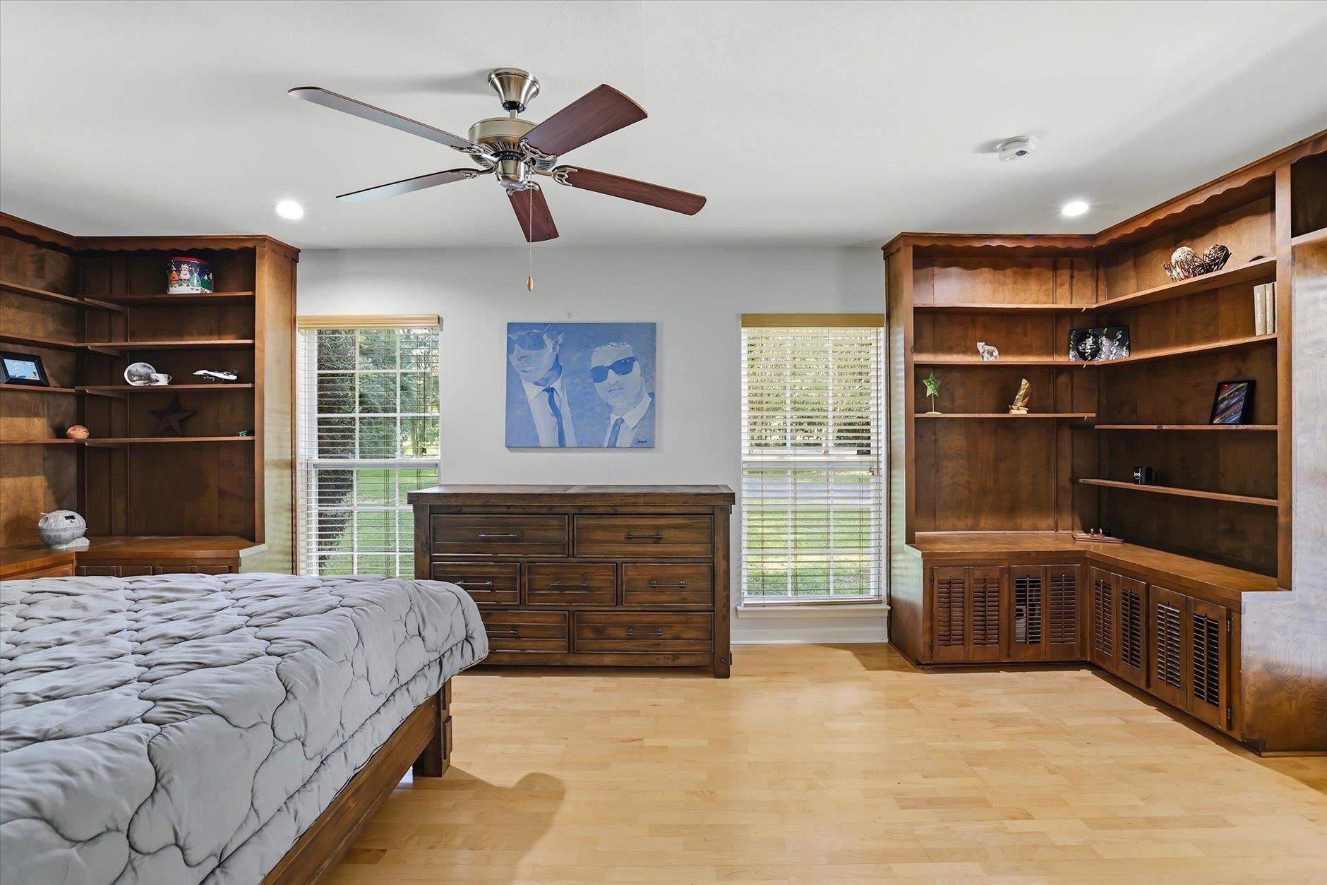 Bedroom with extensive dark wood built-in shelving, a matching dresser, and a bed beneath a ceiling fan.