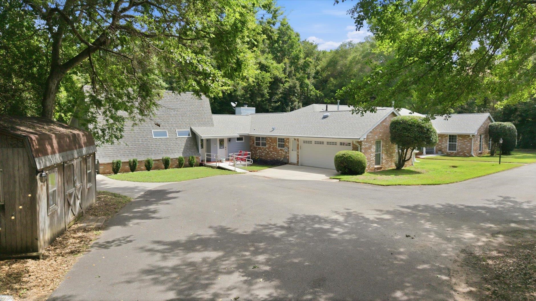 Brick ranch home with attached garage and front ramp, shaded by mature trees.