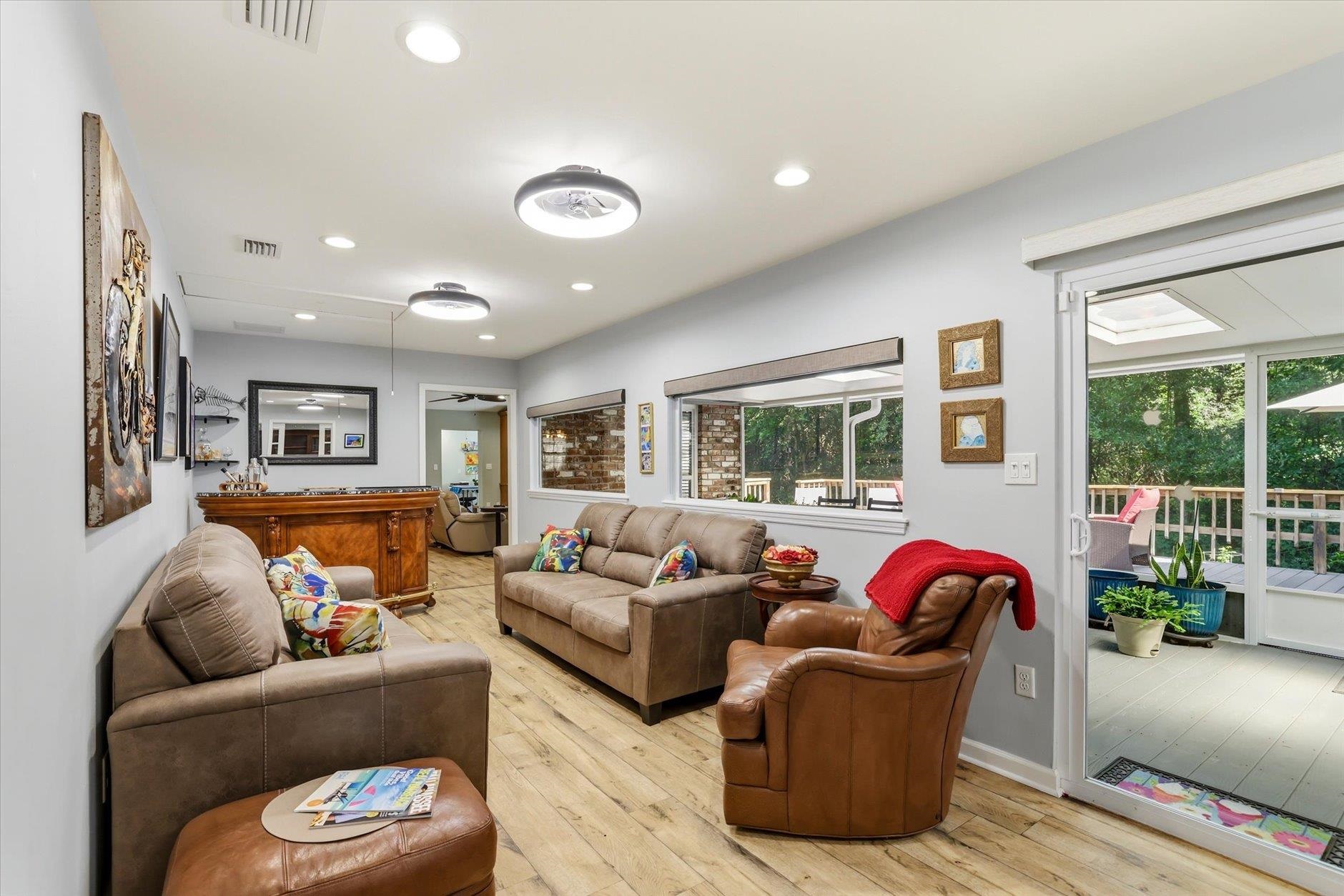 Living room with leather seating, light wood-look floors, and sliding doors to an enclosed porch.
