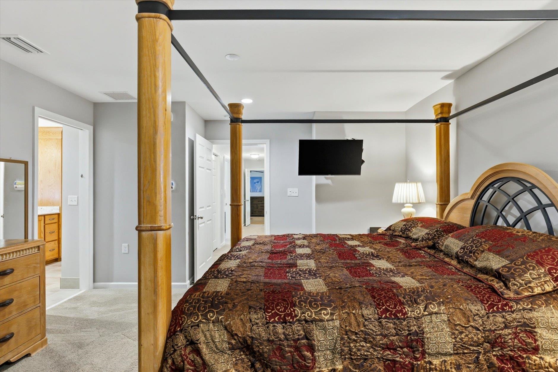 Bedroom with a wooden four-poster bed, ornate patterned bedding, and a wall-mounted television.