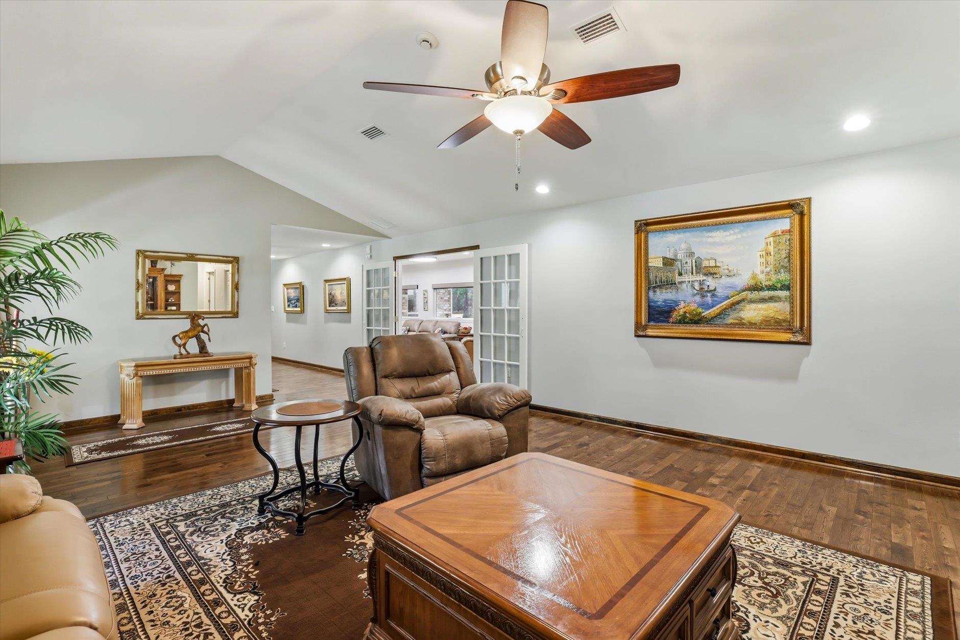 Furnished living room with leather recliners, hardwood floors, and open French doors.