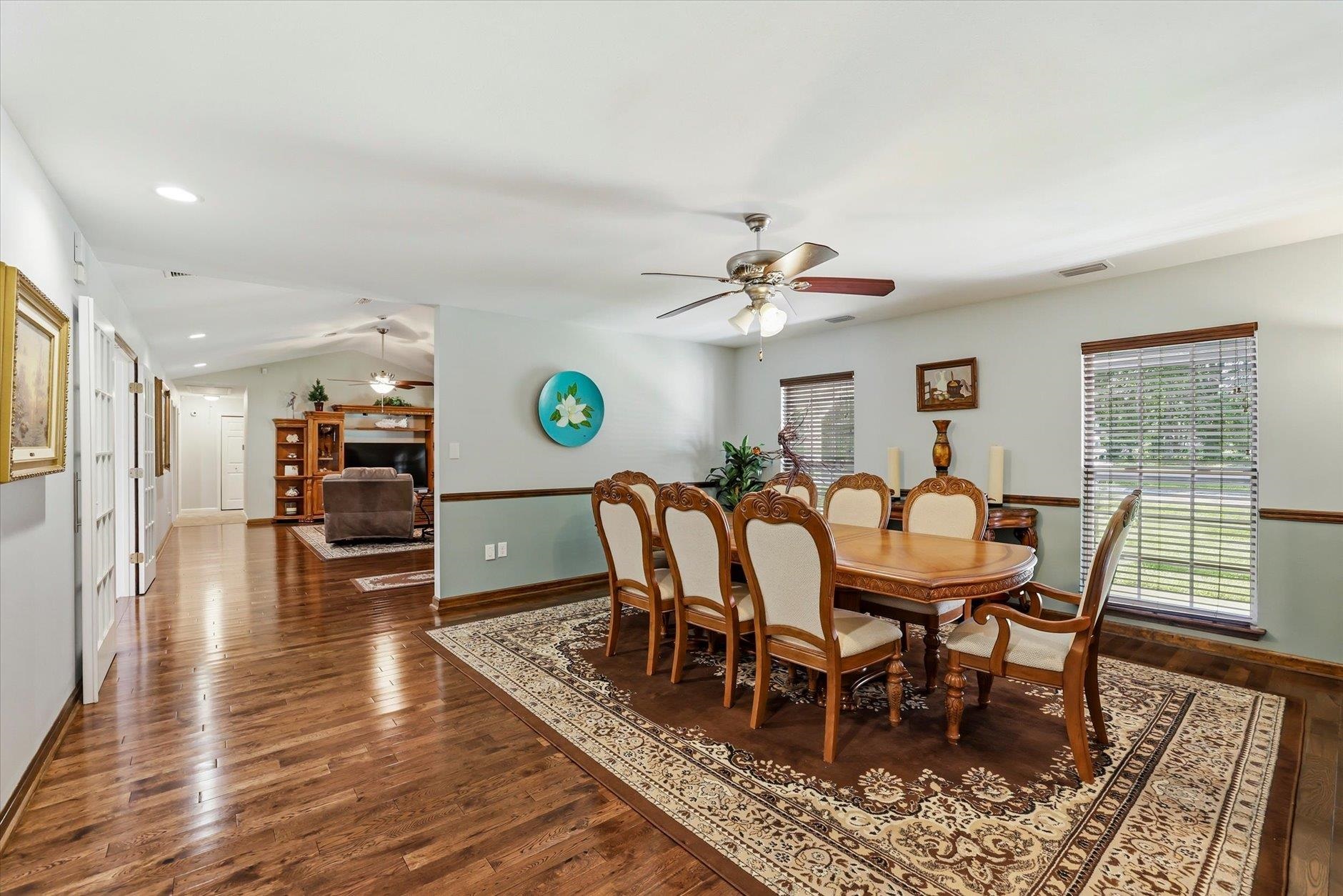 Dining room with an ornate wooden table, upholstered chairs, patterned rug, and adjoining living area.