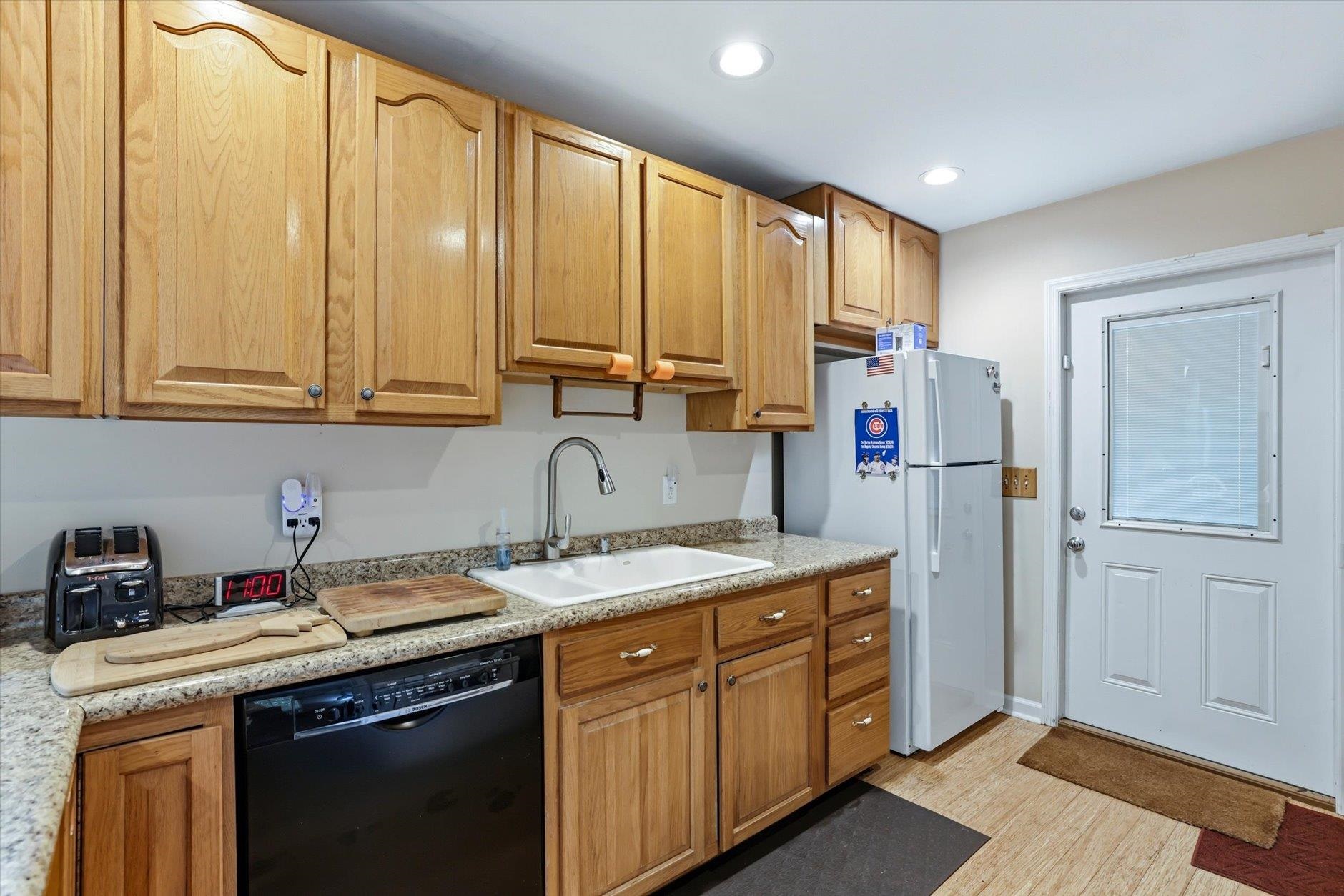 Kitchen with honey-colored wood cabinets, granite counters, and a white sink beside the back door.